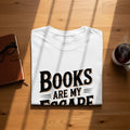 White t-shirt with "Books are my escape" text, notebook, glasses, and steaming mug.