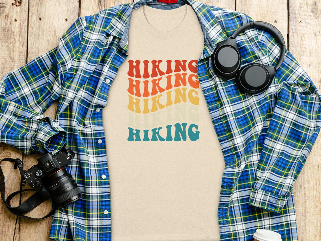 Beige t-shirt with "HIKING" in retro rainbow text, layered over plaid shirt.