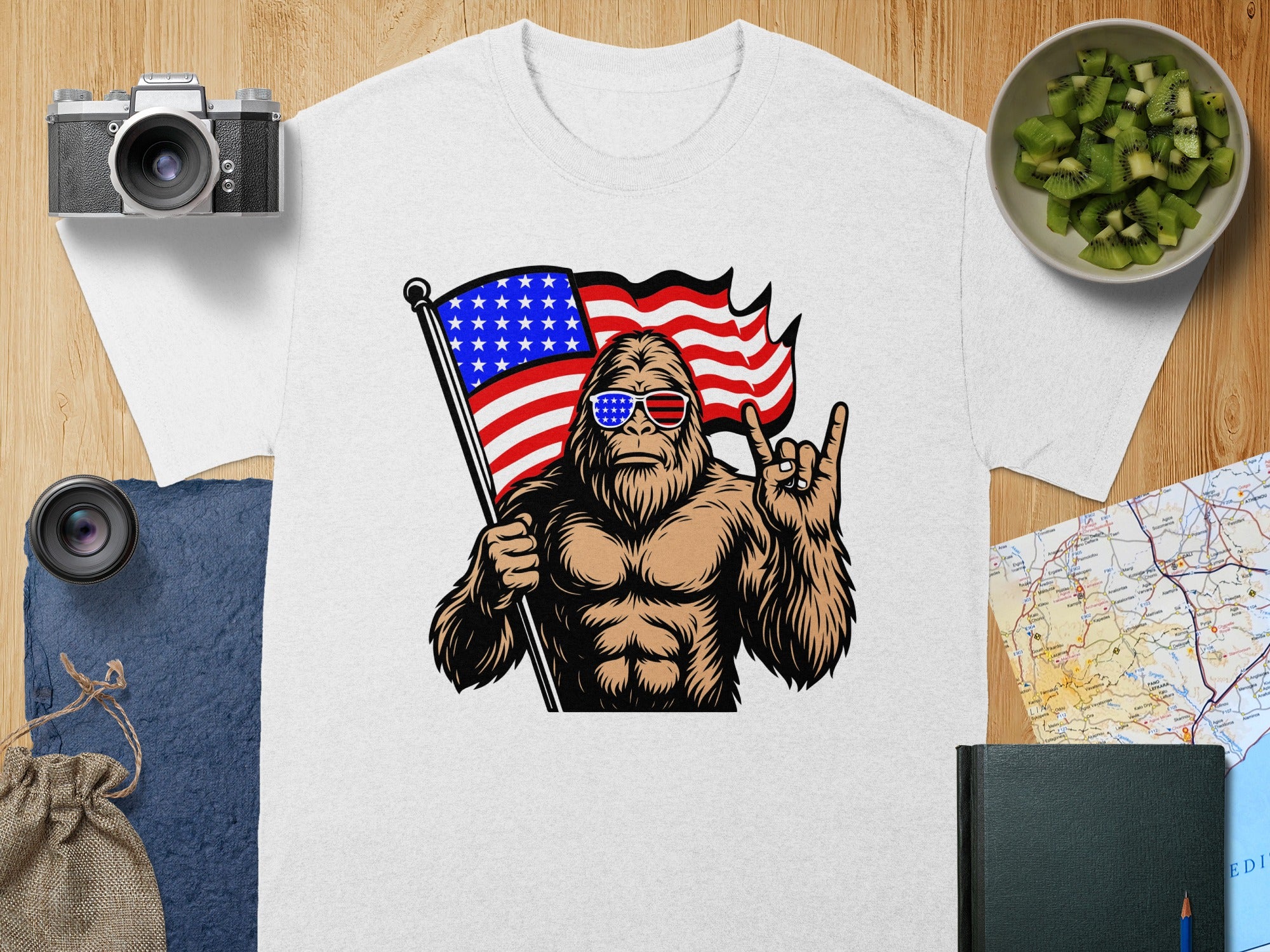 Bigfoot wearing sunglasses, holding an American flag, and making a rock-on hand gesture.