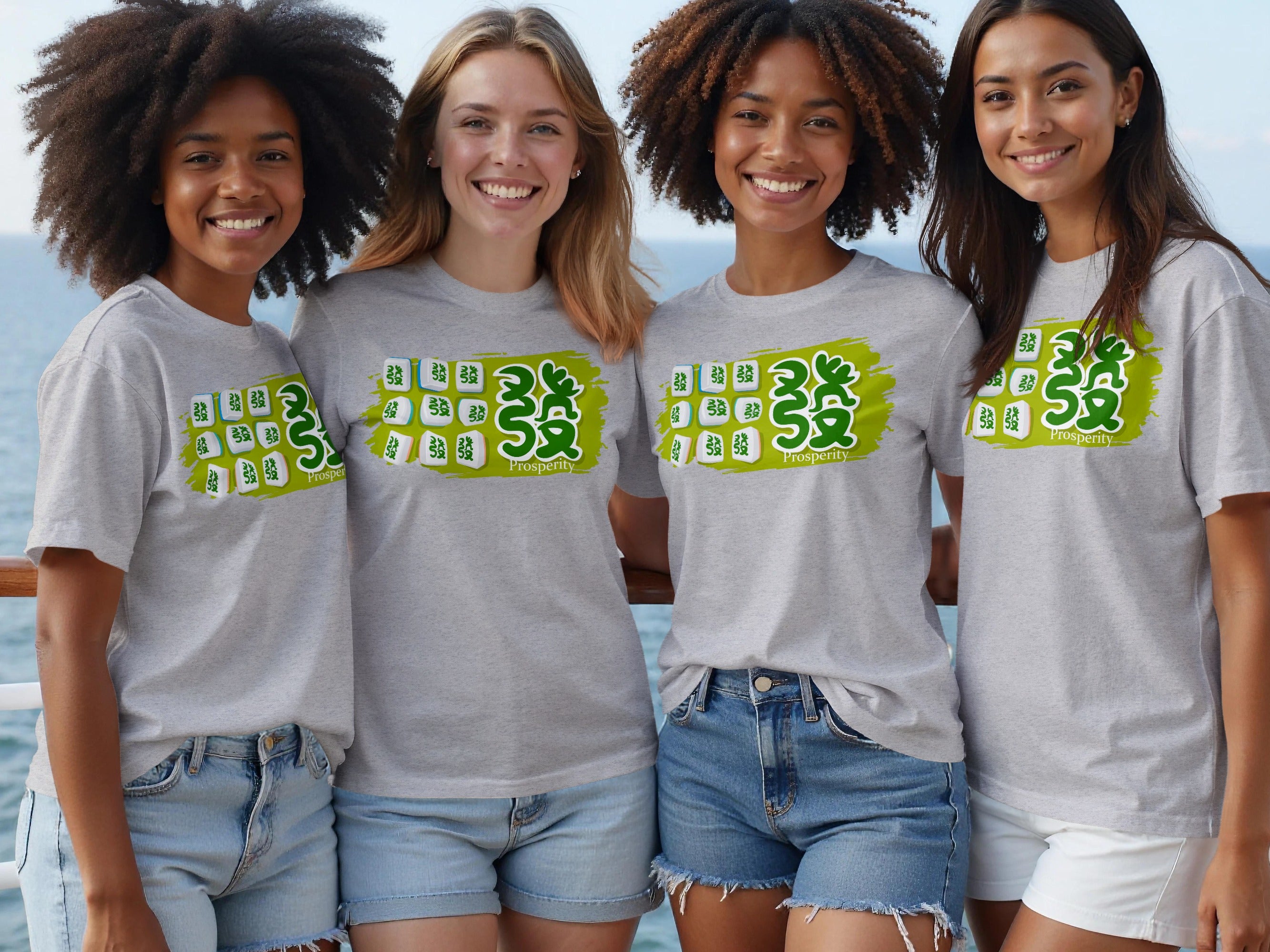 Four smiling women wear grey t-shirts with a green graphic and mahjong tiles featuring Chinese characters.