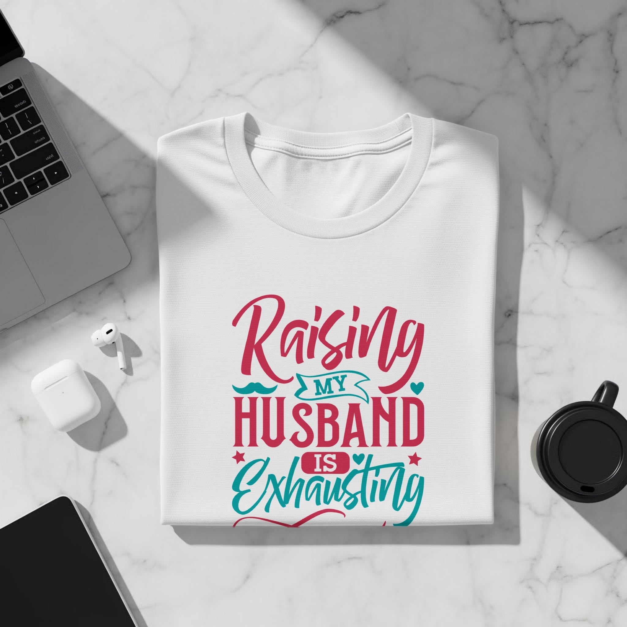 White t-shirt with "Raising my husband is exhausting" text in pink and teal.