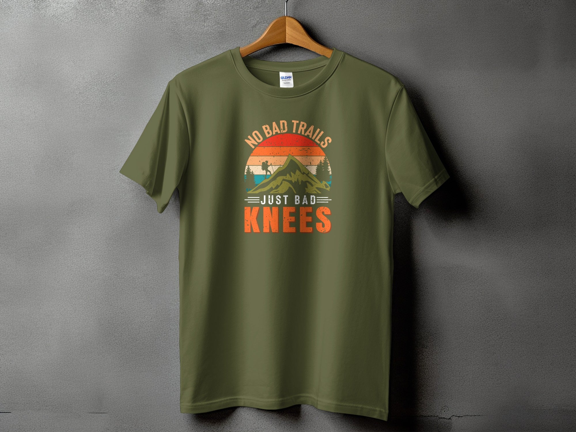 Olive green t-shirt with "No Bad Trails Just Bad Knees" mountain graphic.