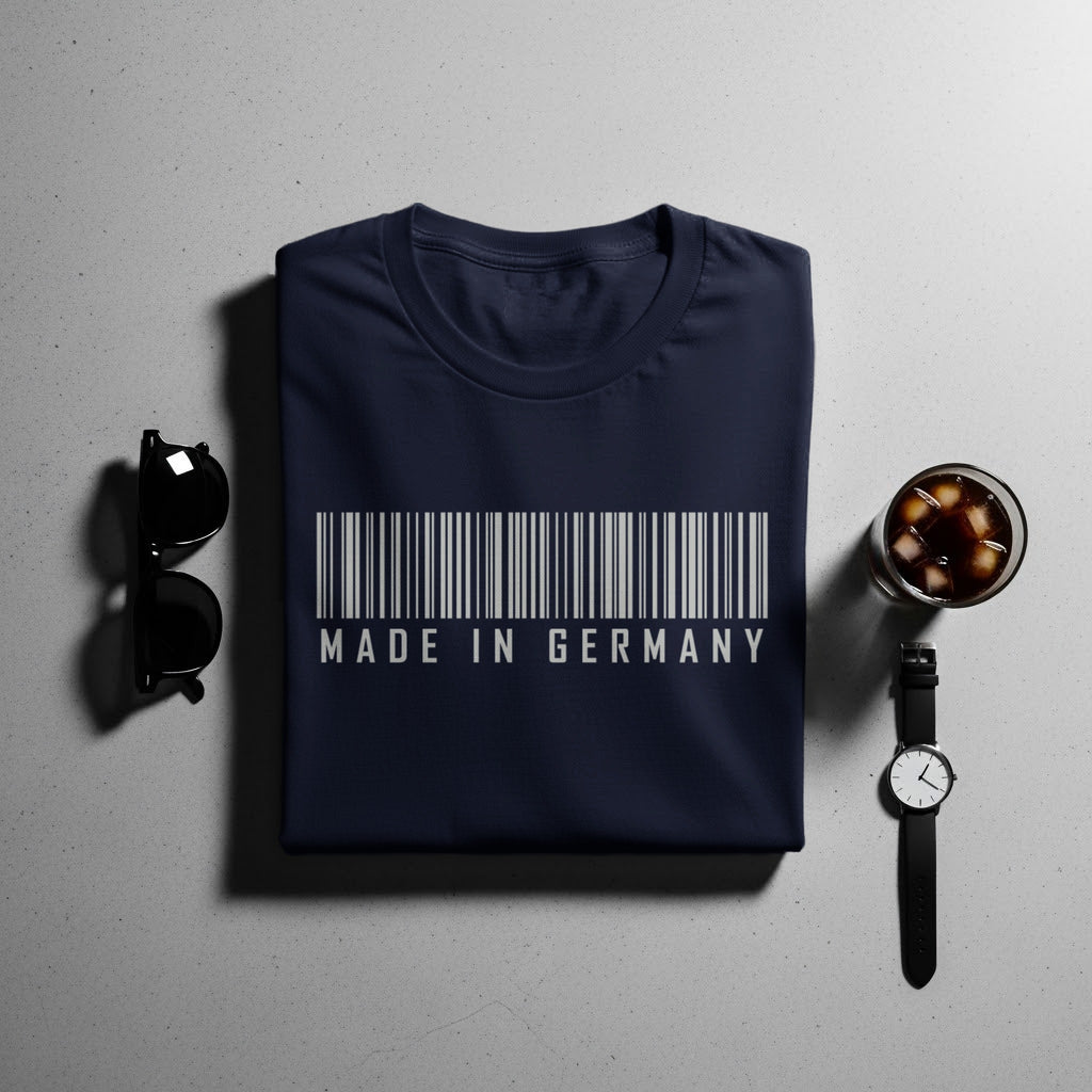 Navy t-shirt with barcode and "Made in Germany" text, with sunglasses, drink, and watch.