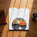 White t-shirt with a circular graphic of mountains and a tent, depicting day and night.