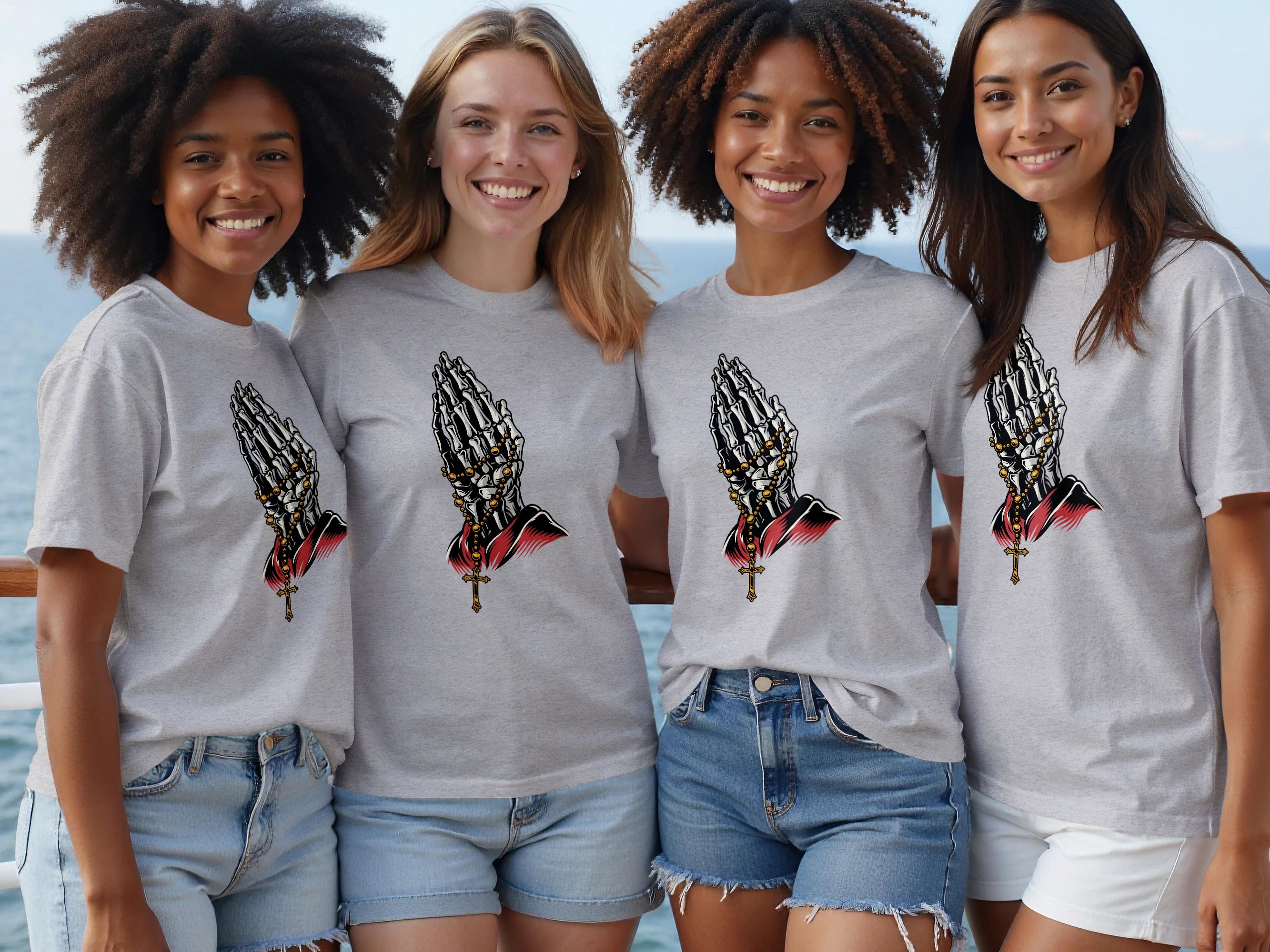 Four smiling women wear gray t-shirts featuring a skeleton hand prayer design.