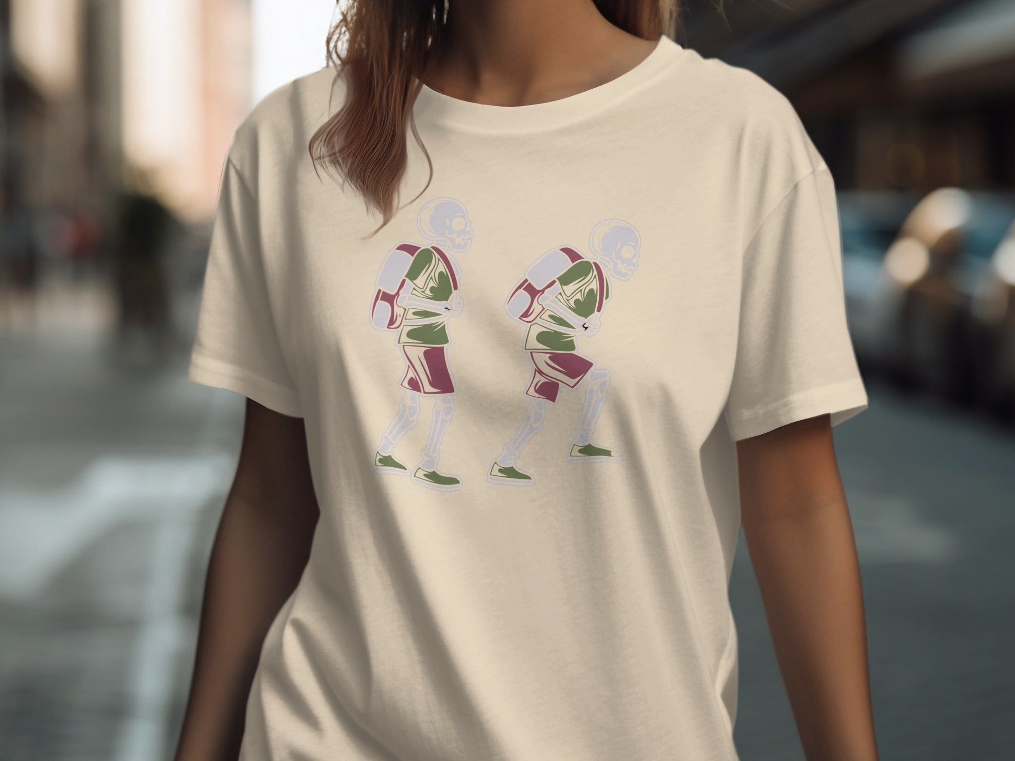Two skeletons with backpacks walk forward on a cream t-shirt.
