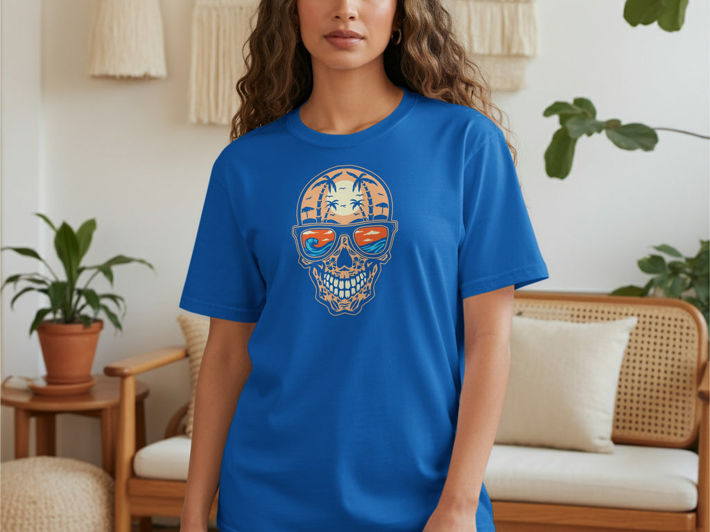 Blue t-shirt with a skull graphic featuring a tropical beach sunset reflection in sunglasses.