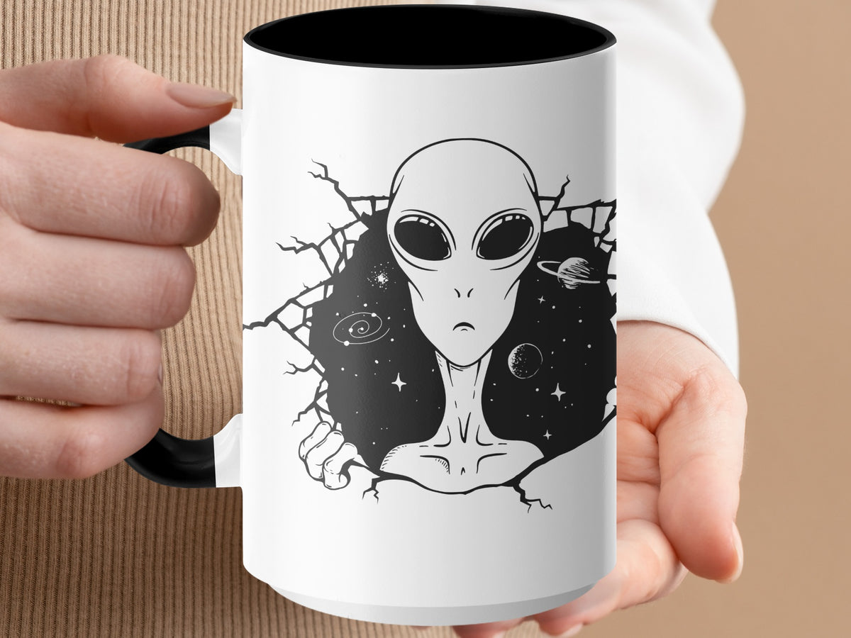 White mug with black interior featuring a cracked space scene with an alien head and planets.