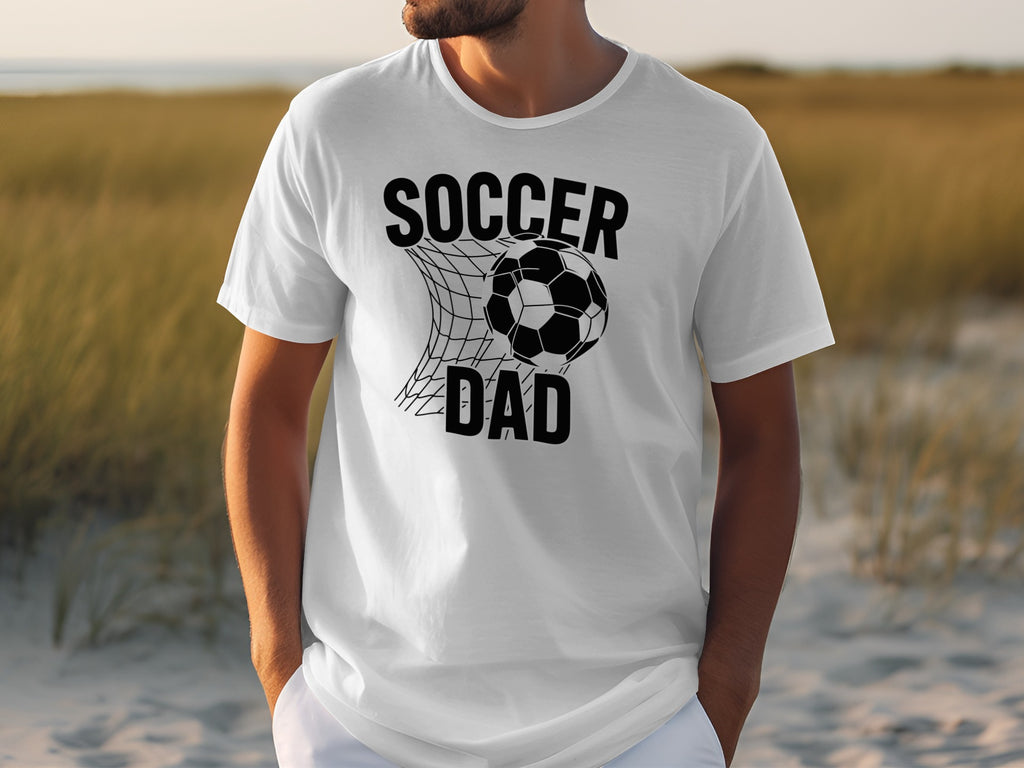 White t-shirt with black text and graphics that read "Soccer Dad" and a soccer ball in a net.