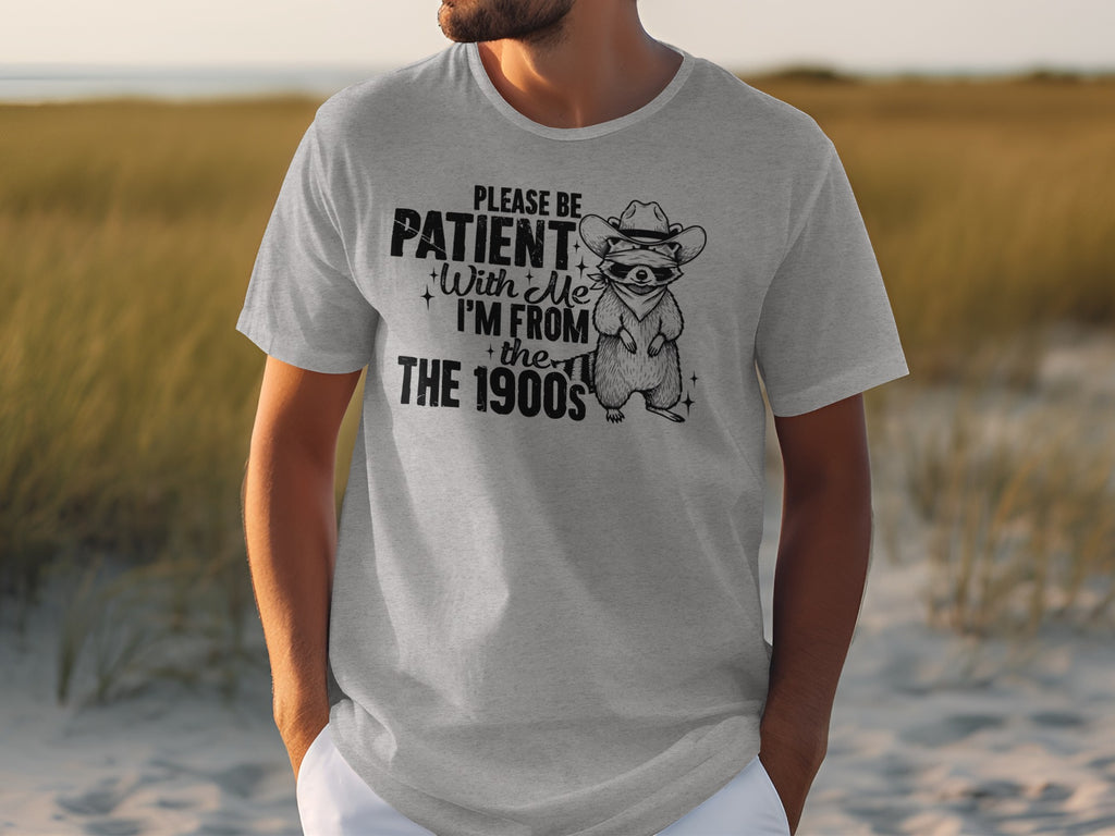 Grey t-shirt with a raccoon wearing a cowboy hat and bandana and text saying "Please be patient with me I'm from the 1900s".
