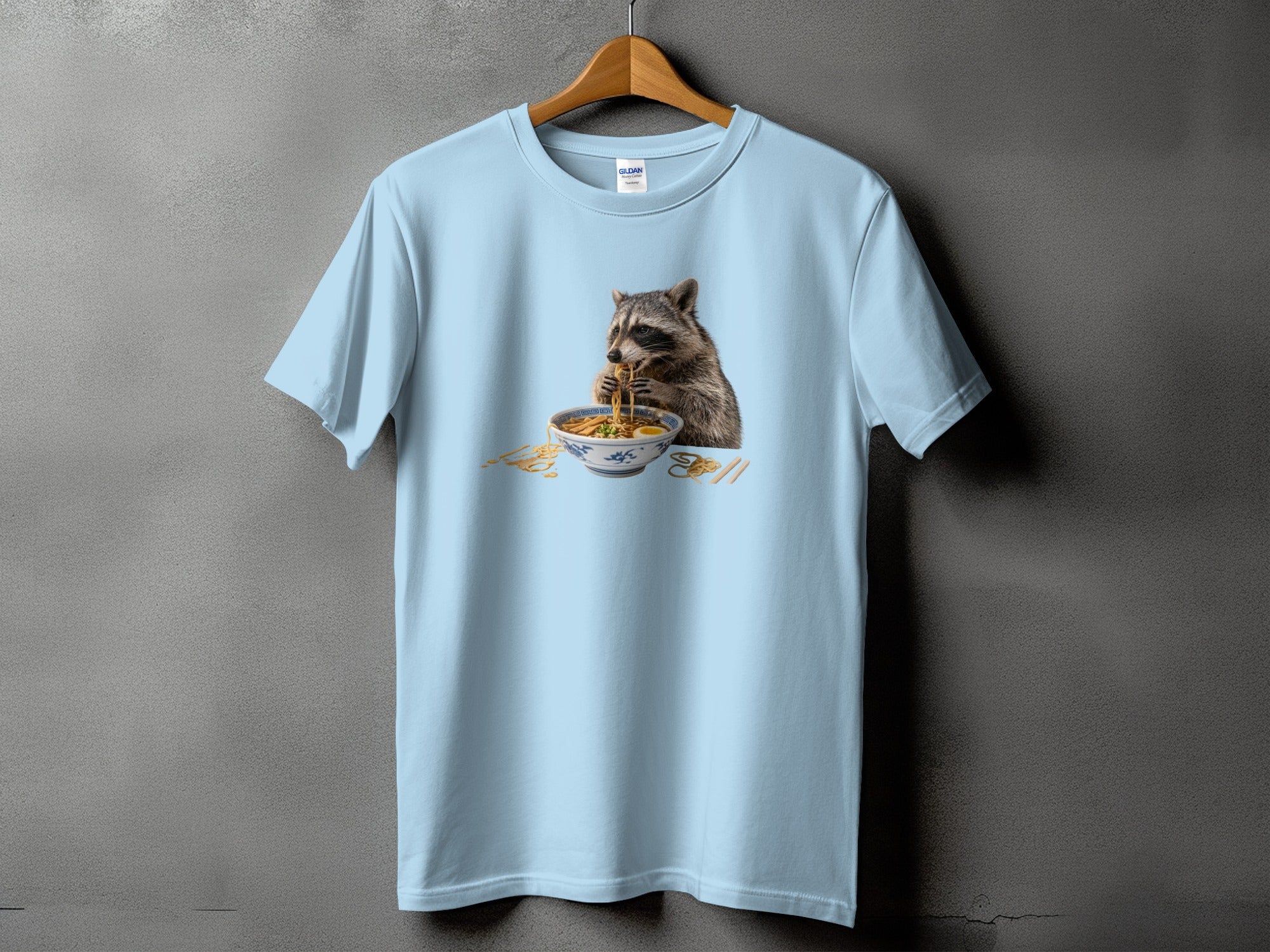 Light blue t-shirt with a graphic of a raccoon eating ramen.