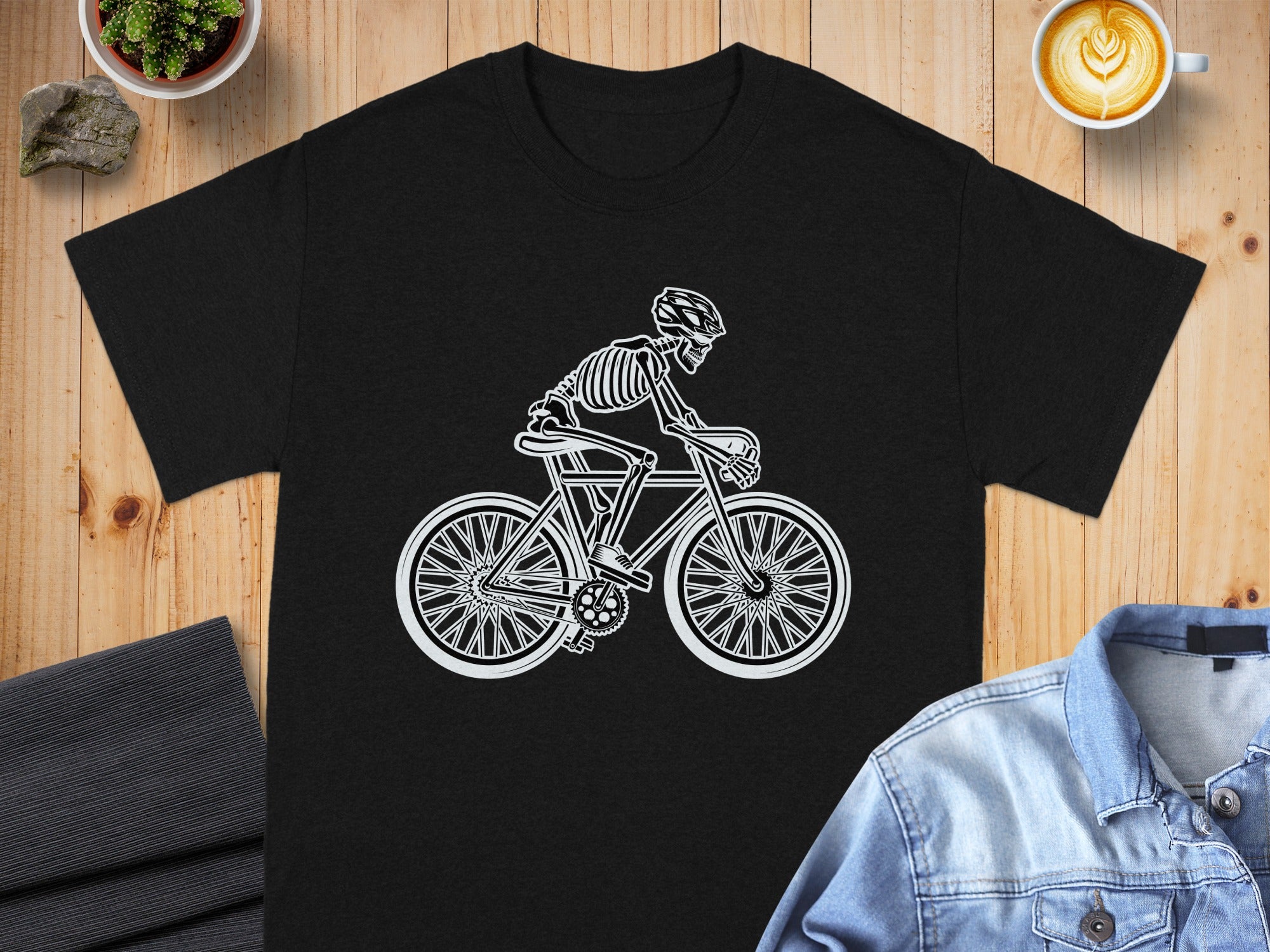 Black t-shirt with white skeleton cyclist graphic on wooden background.