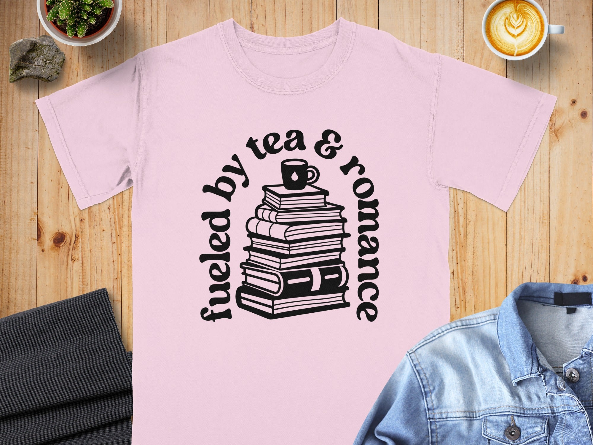Pink t-shirt with black text and graphics of books, a tea cup, and the phrase "fueled by tea & romance".