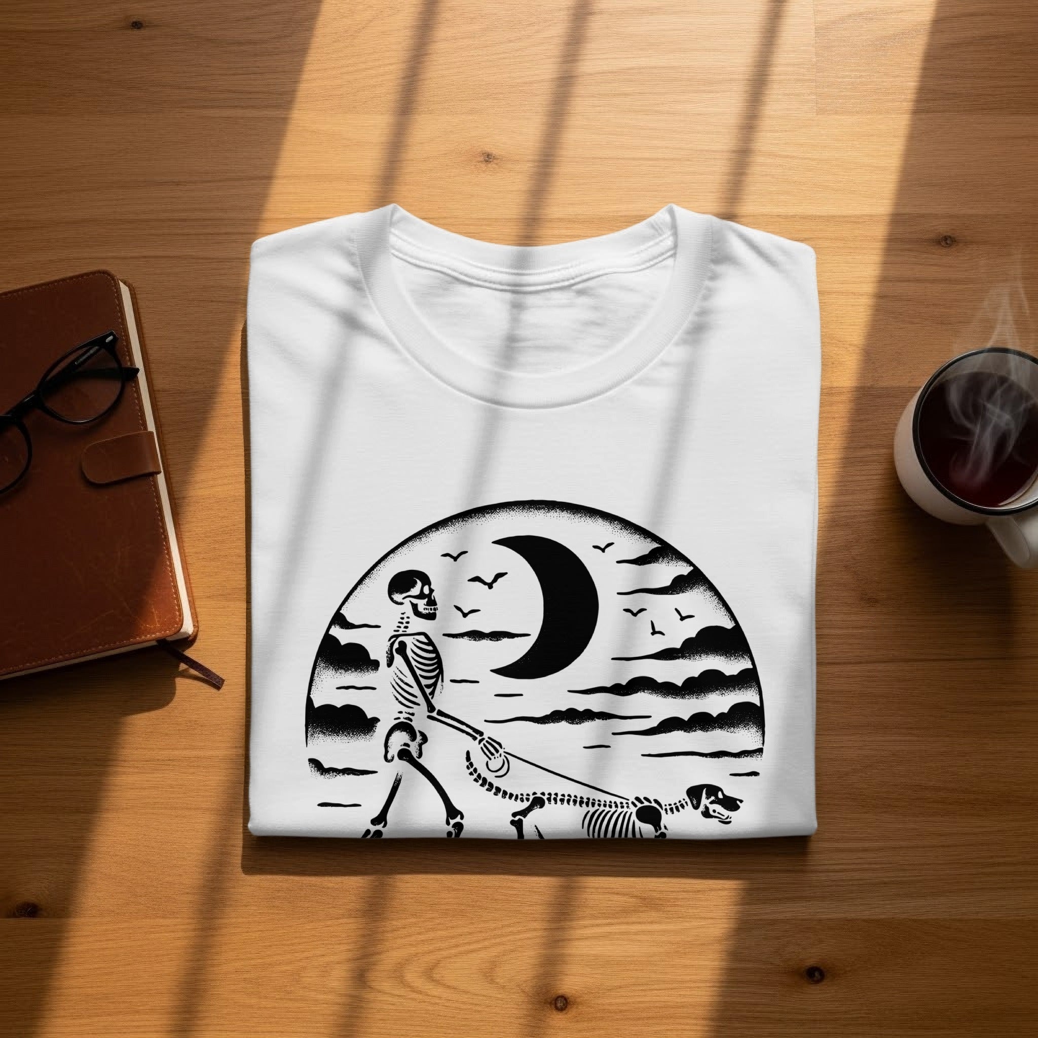 White t-shirt with a black graphic of a skeleton walking a skeleton dog under a crescent moon.