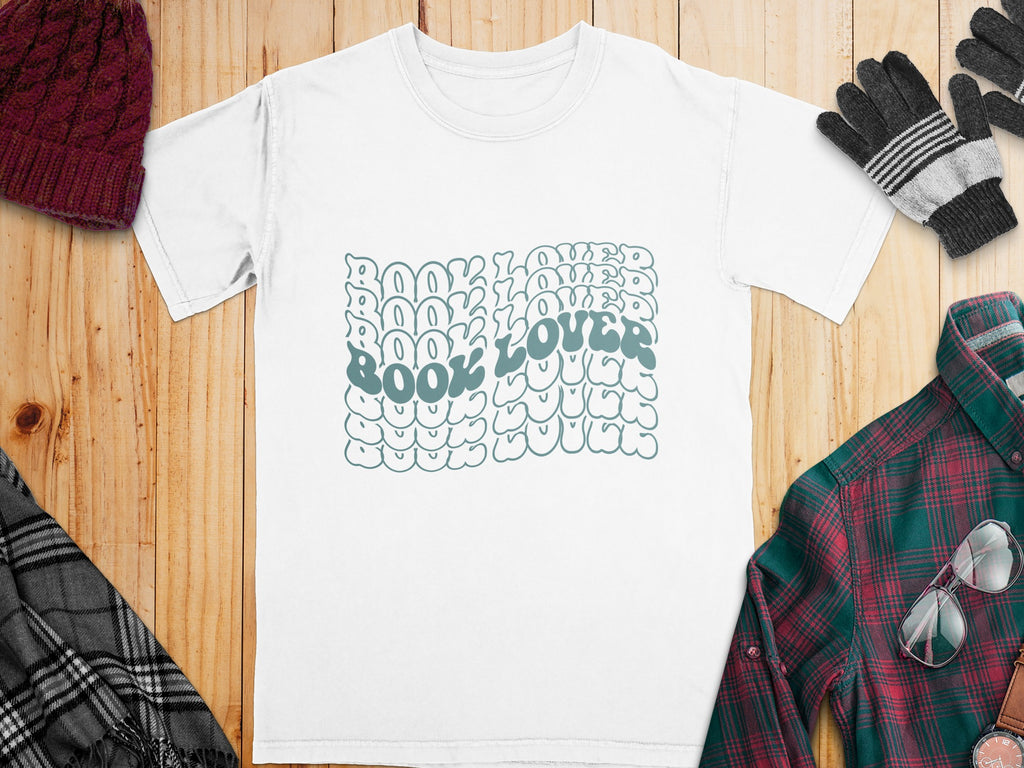 White t-shirt with "BOOK LOVER" text in wavy aquamarine bubble font.