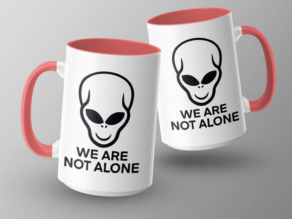 Two white mugs with red interiors and handles, featuring alien faces and "WE ARE NOT ALONE" text.