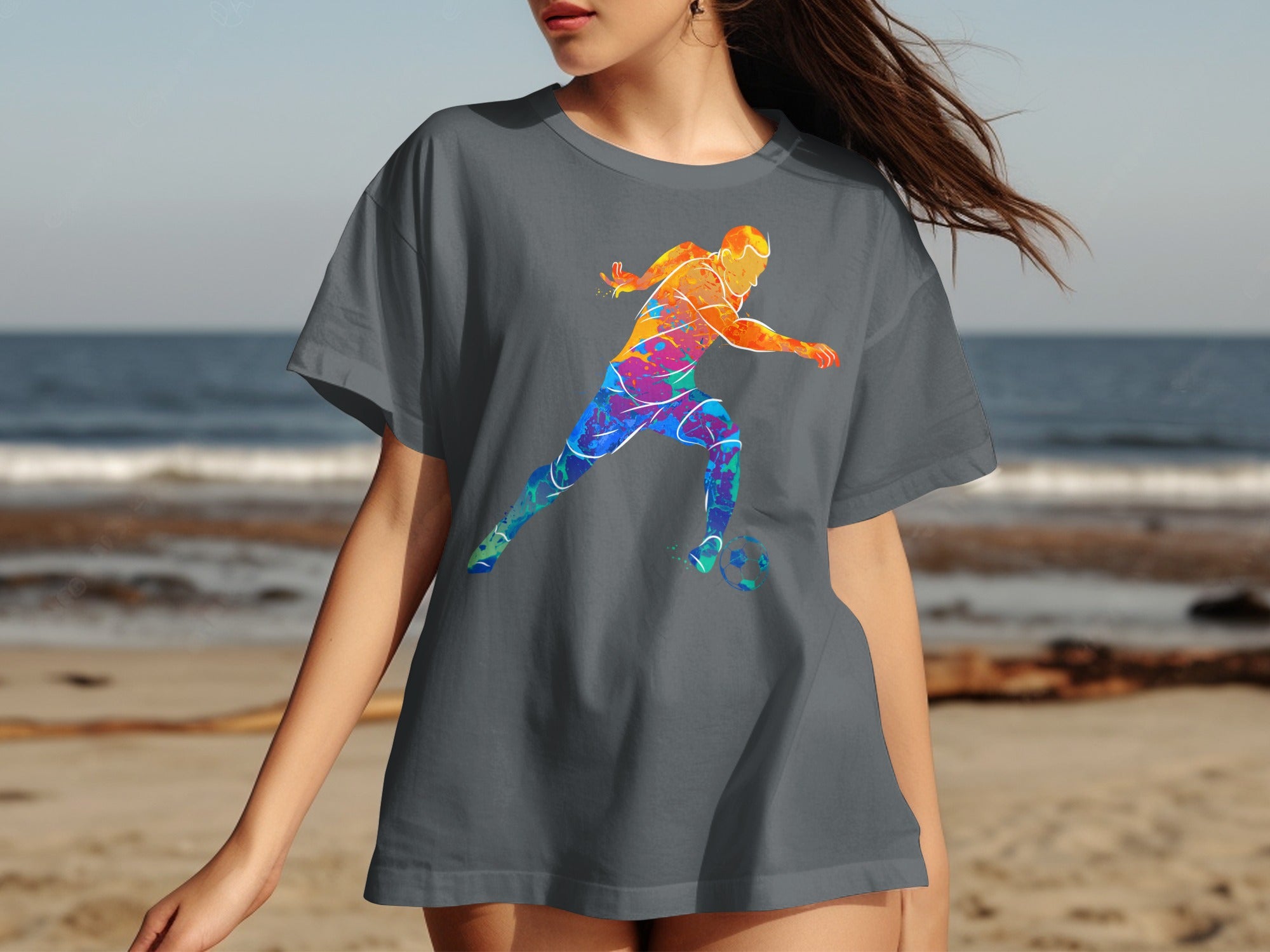 A gray t-shirt with a colorful abstract soccer player graphic on a beach.