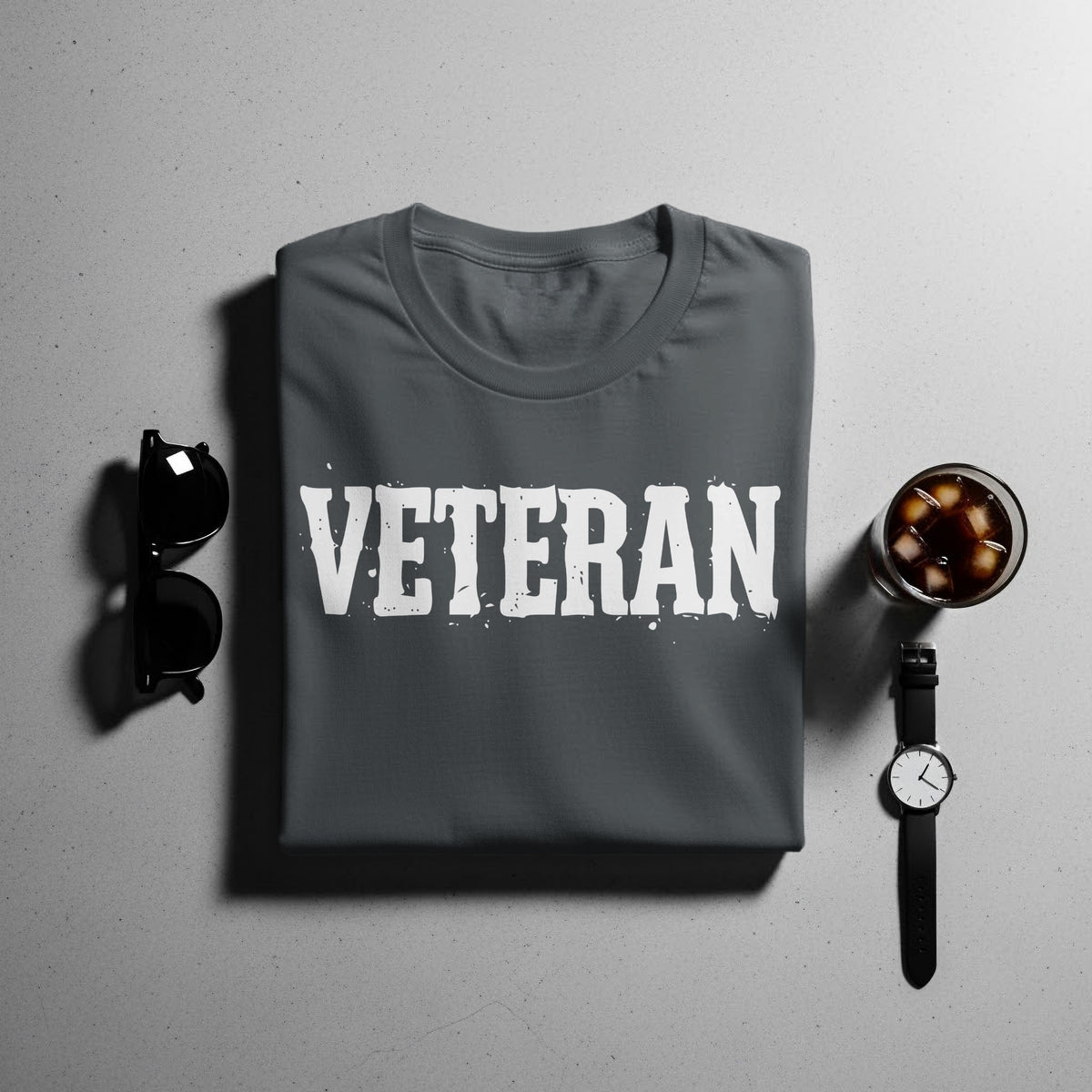 Dark grey t-shirt with white "VETERAN" text, sunglasses, watch, and drink.