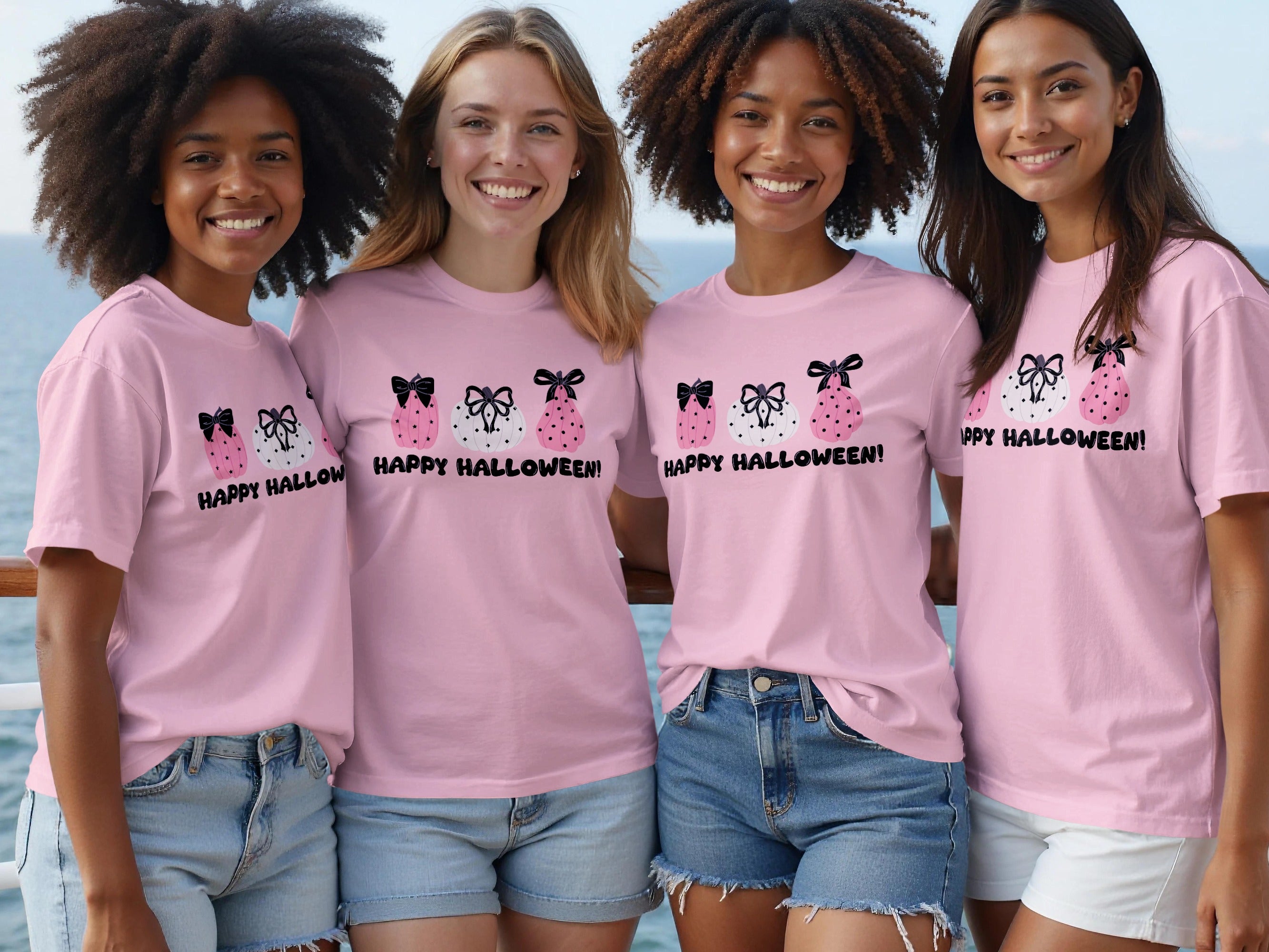 Four smiling women wear pink t-shirts with Halloween pumpkin designs and text.