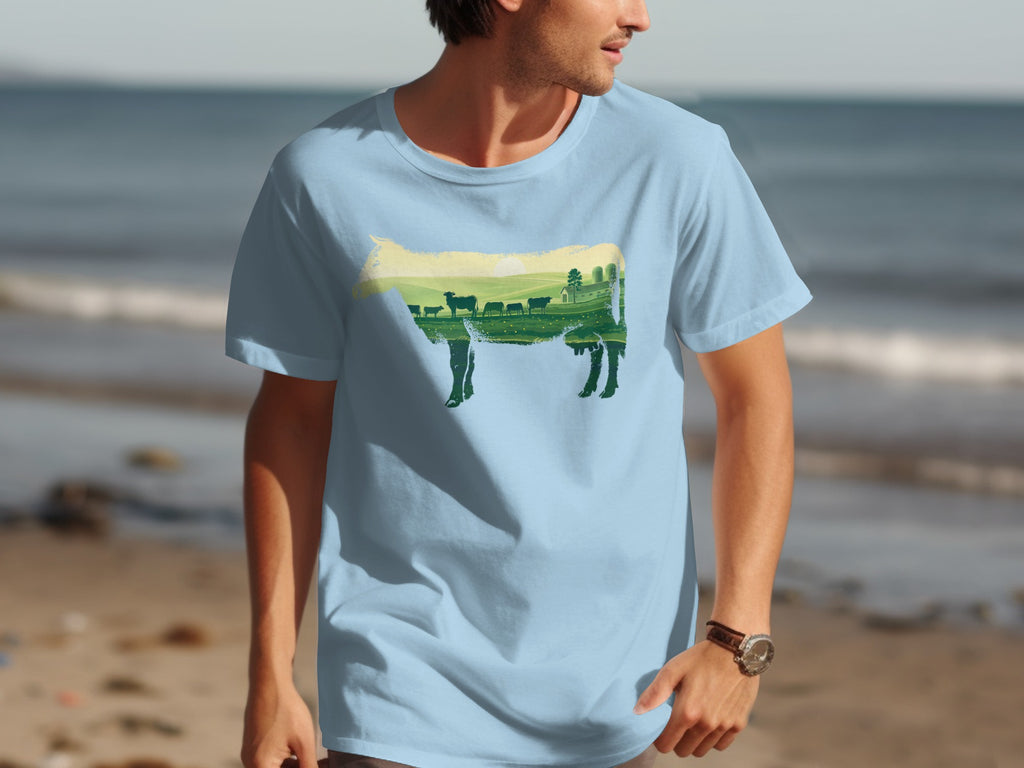 Light blue t-shirt with a cow silhouette filled with a countryside landscape and farm scene.