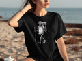 Black t-shirt with a skeleton hiker graphic, set against a beach background.