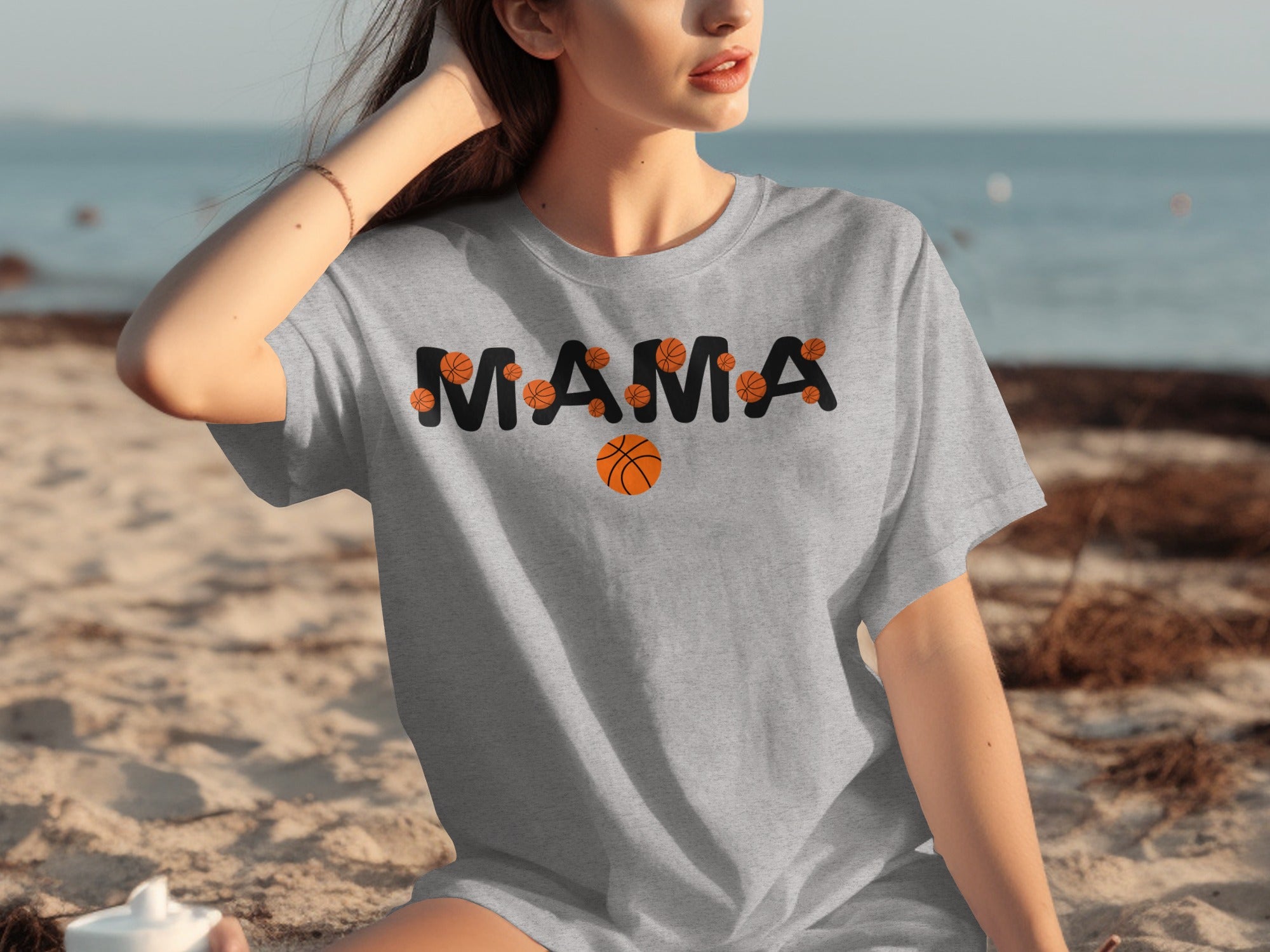 Grey t-shirt with black "MAMA" text and basketball graphics on a beach.