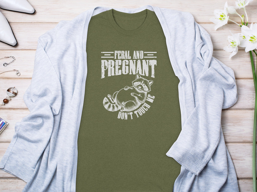 Olive t-shirt with white text "FERAL AND PREGNANT DON'T TOUCH ME" and raccoon graphic.