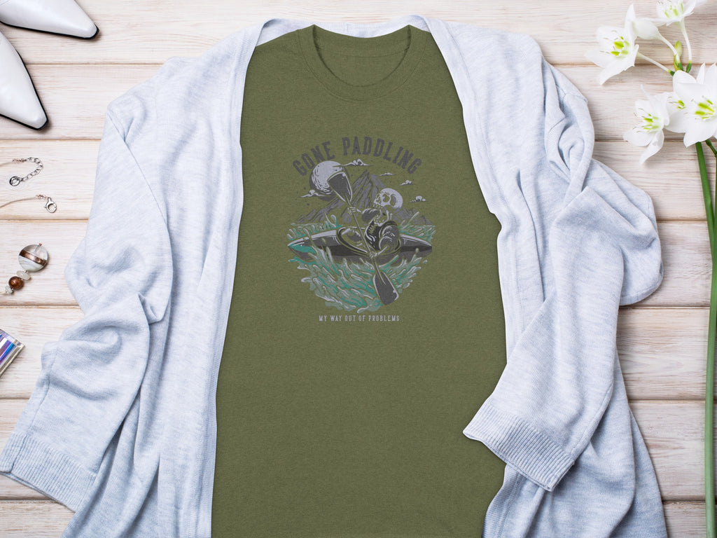 Olive t-shirt graphic with skeleton kayaking and text "GONE PADDLING MY WAY OUT OF PROBLEMS".