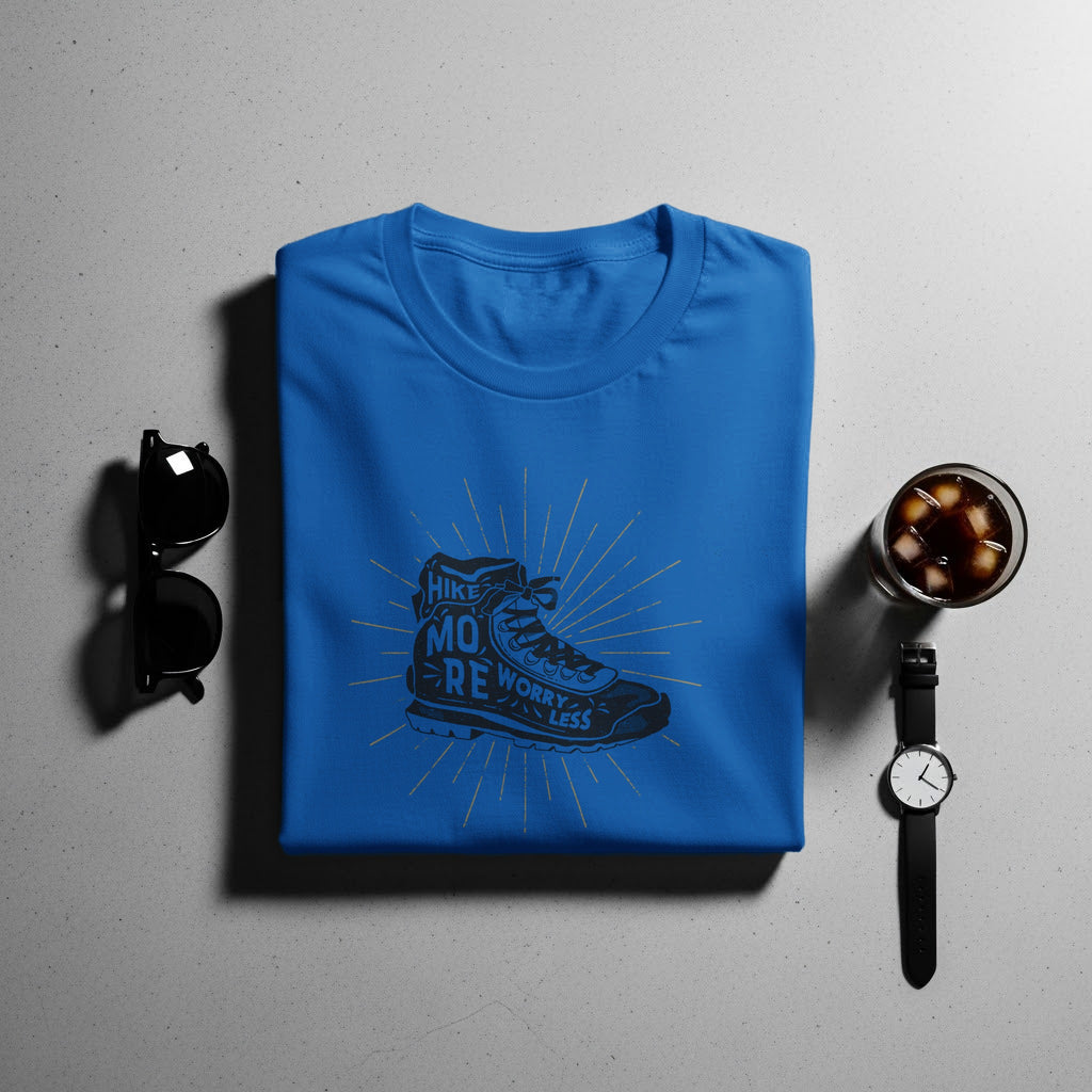 Blue t-shirt with "Hike More Worry Less" hiking boot graphic, sunglasses, watch, and drink.