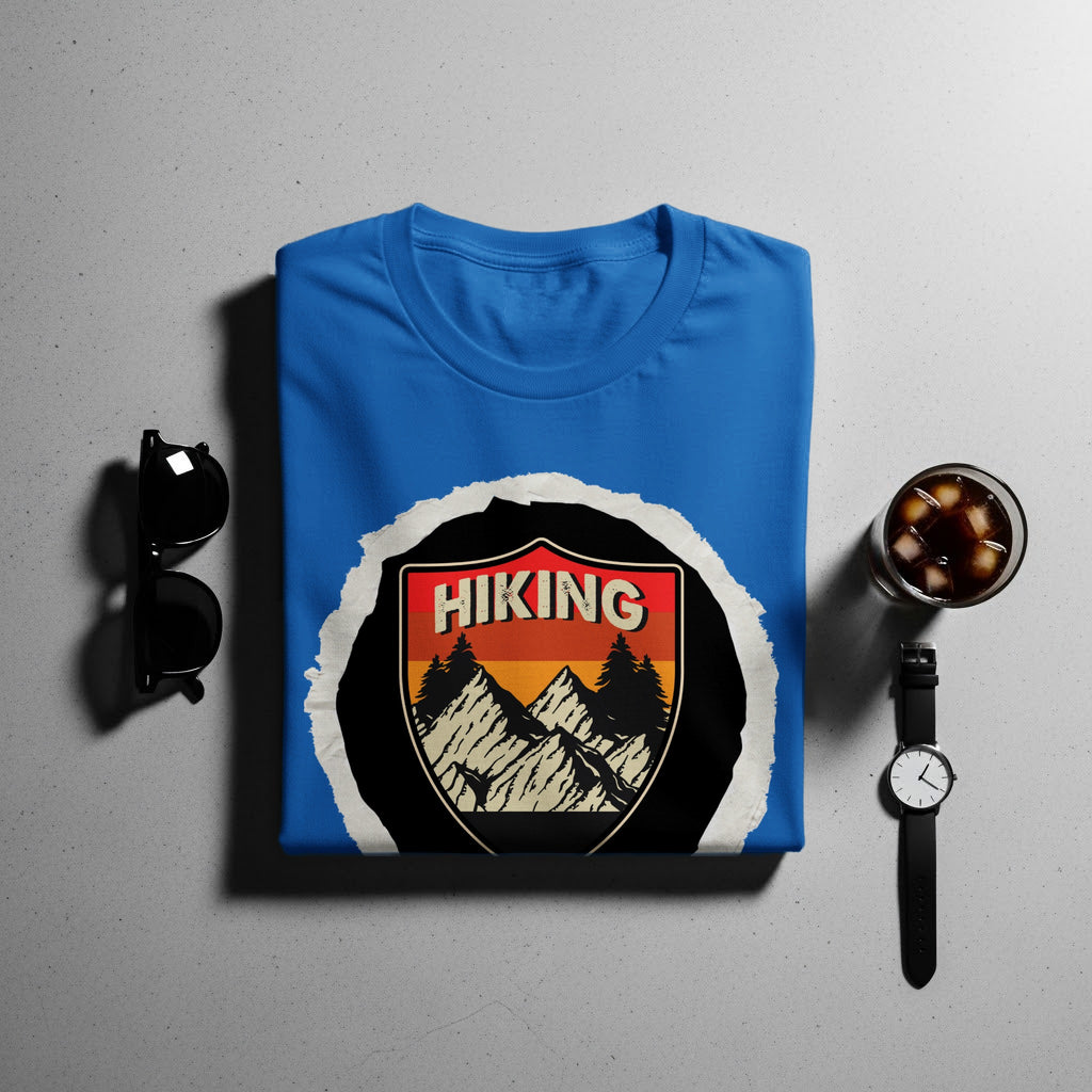 Blue t-shirt with "Hiking" mountain badge design, displayed with sunglasses and watch.