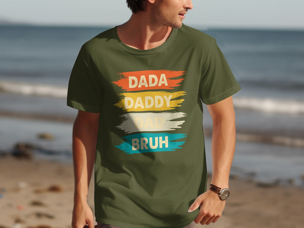 Olive green t-shirt with text "DADA DADDY DAD BRUH" in distressed, colorful brush strokes.