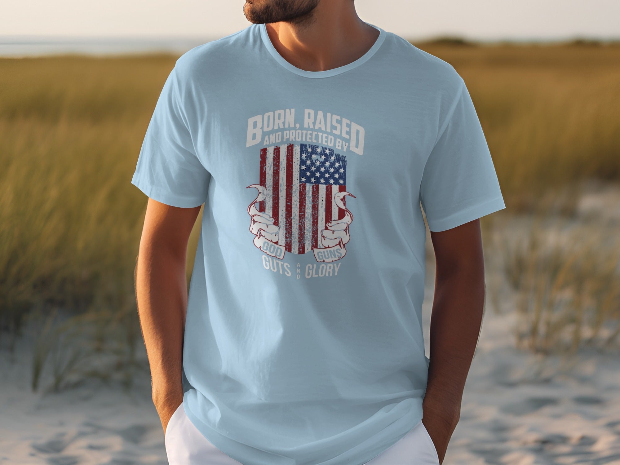 Light blue t-shirt with American flag graphic and text reading "Born, Raised And Protected By God, Guns, Guts & Glory".