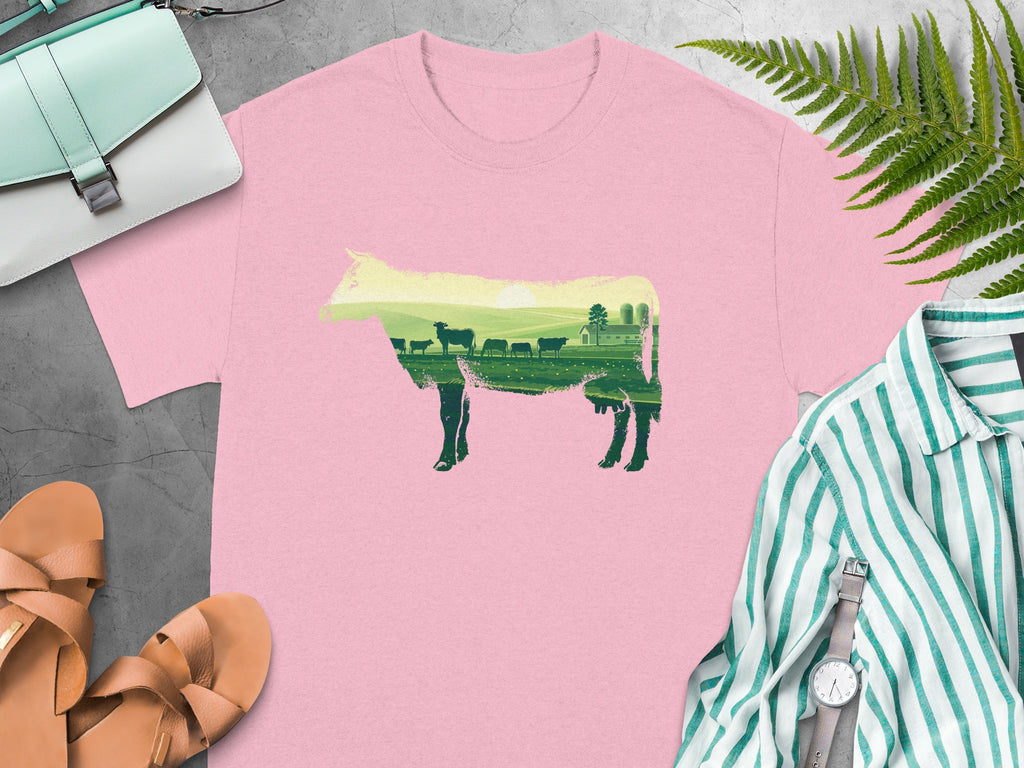 Pink t-shirt with a cow silhouette filled with a farm landscape at sunset.