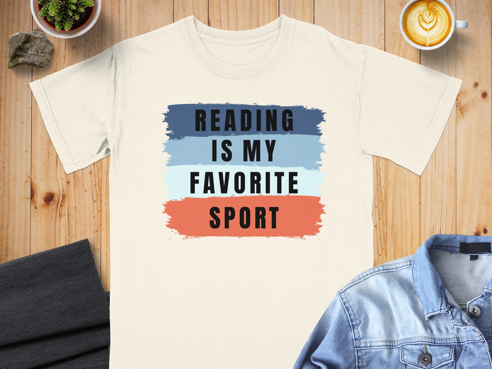 Cream t-shirt with "READING IS MY FAVORITE SPORT" text on colored brush strokes.