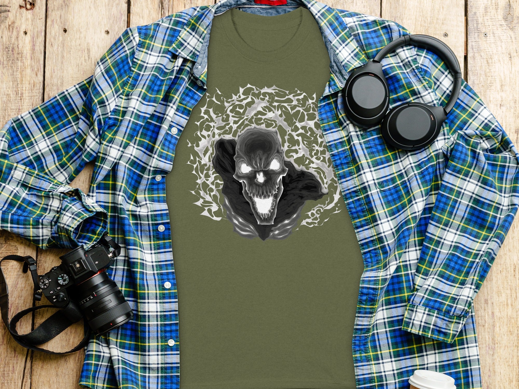 Olive green t-shirt with a black and white skull graphic, layered with a plaid shirt.