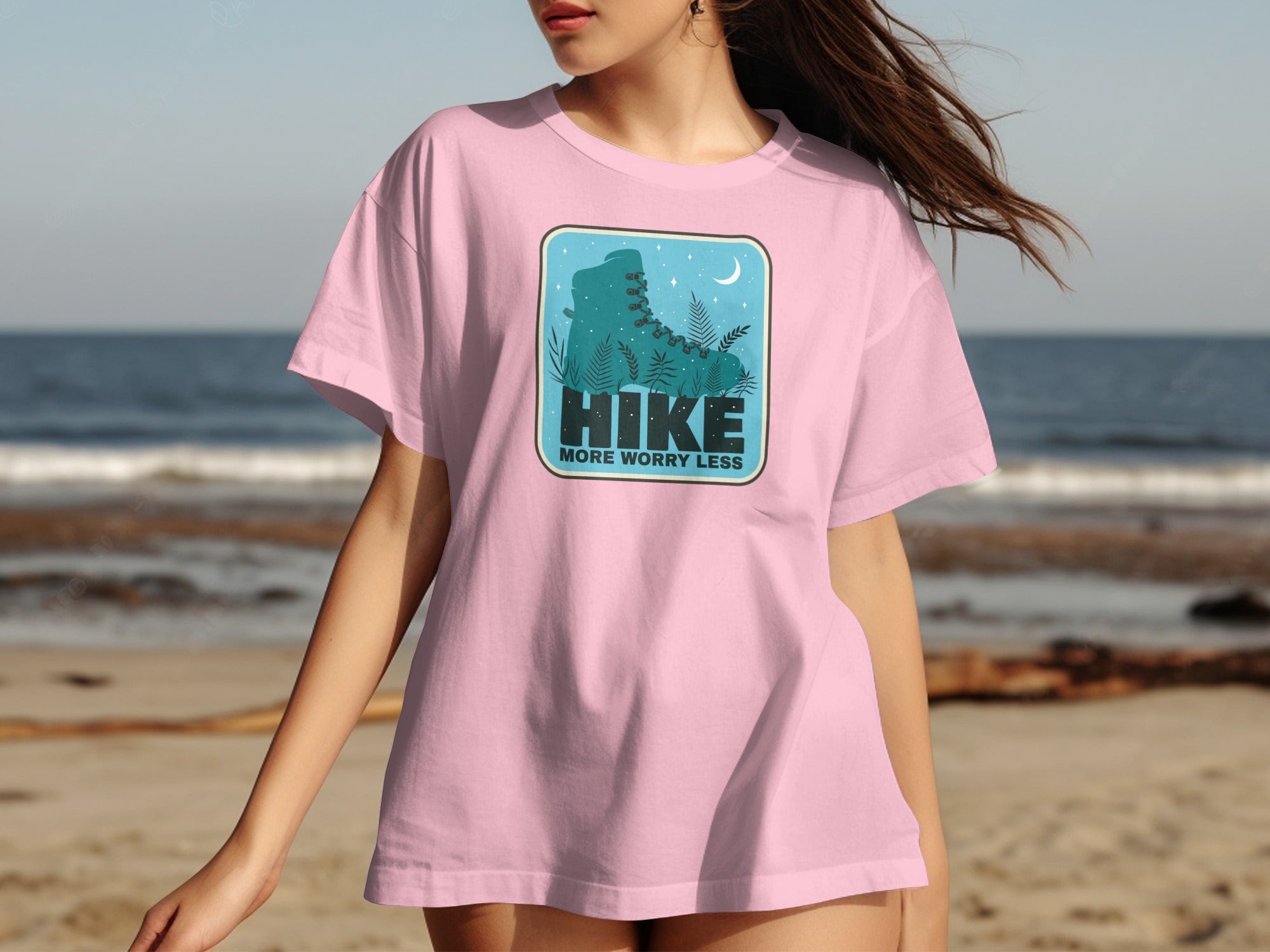 Pink t-shirt with graphic of a teal hiking boot, ferns, and text "HIKE MORE WORRY LESS".