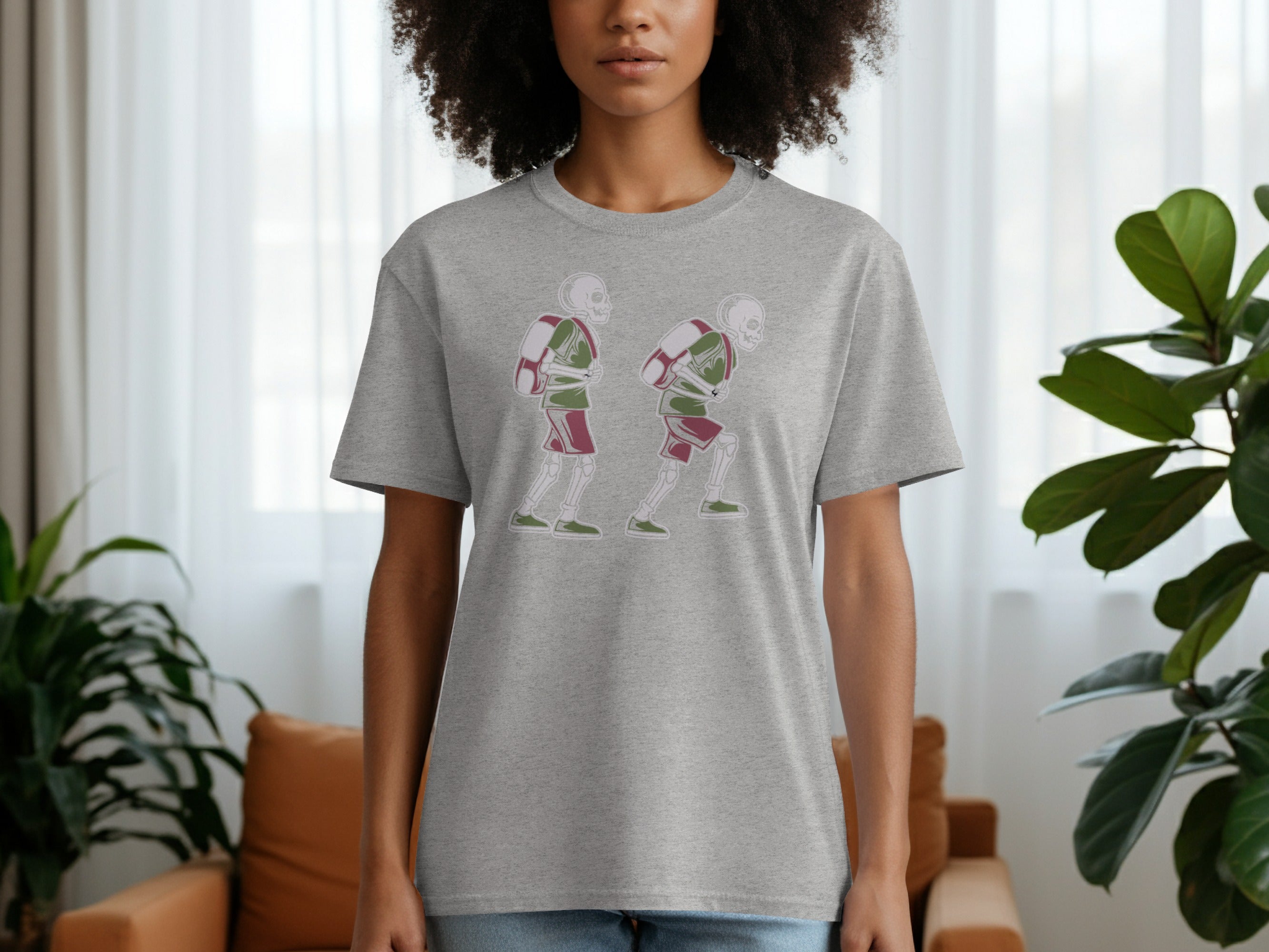 Grey t-shirt with a graphic of two skeletons wearing backpacks and athletic wear.