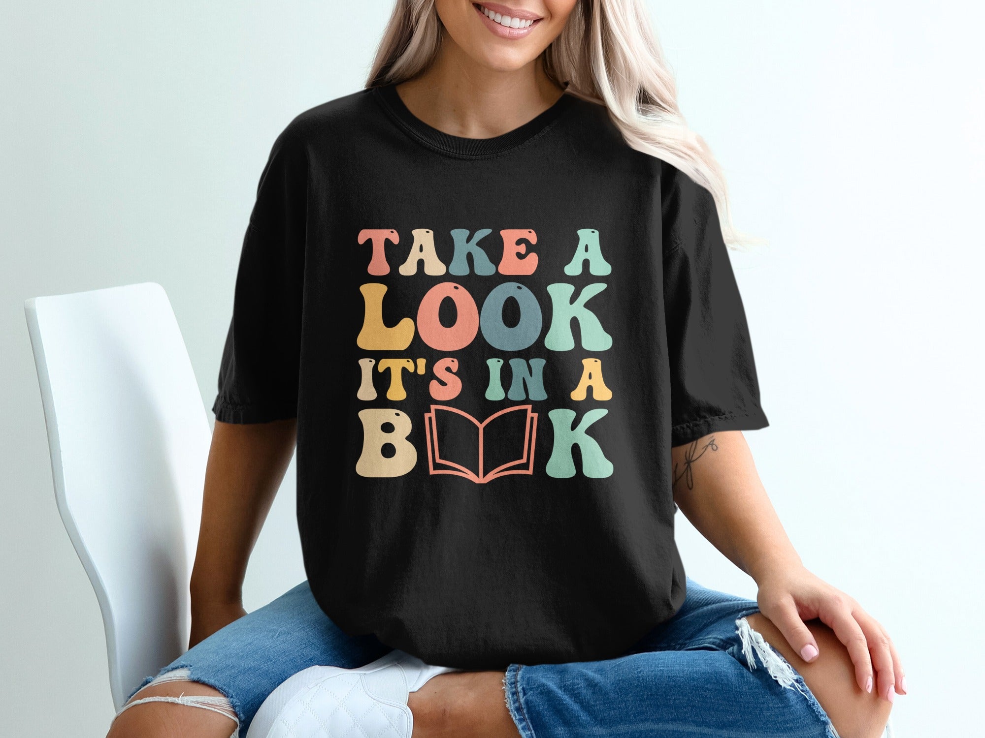 Black t-shirt with text "TAKE A LOOK IT'S IN A BOOK" in colorful retro font.
