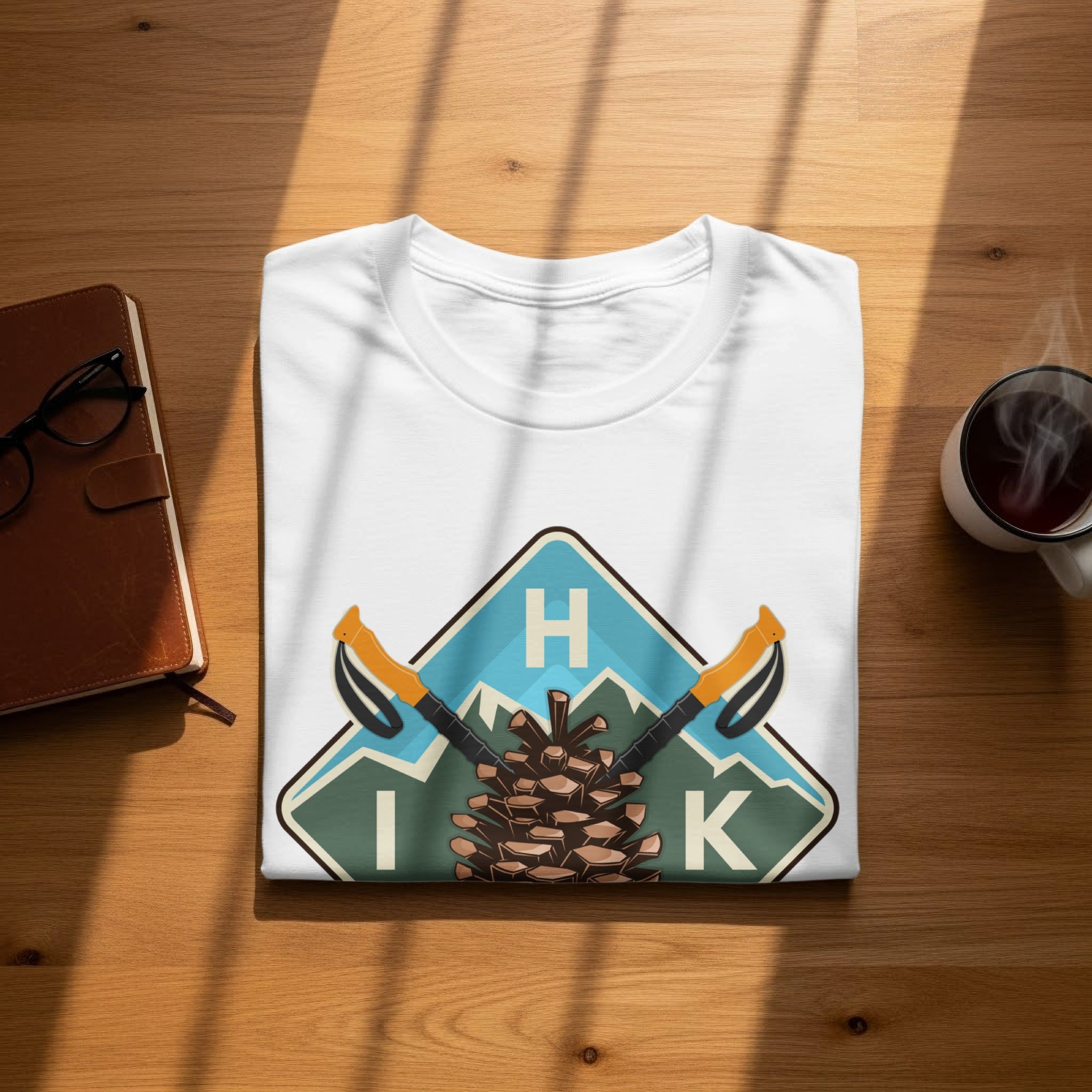 White t-shirt with a nature graphic featuring a pinecone, mountains, ski poles, and letters H I K.