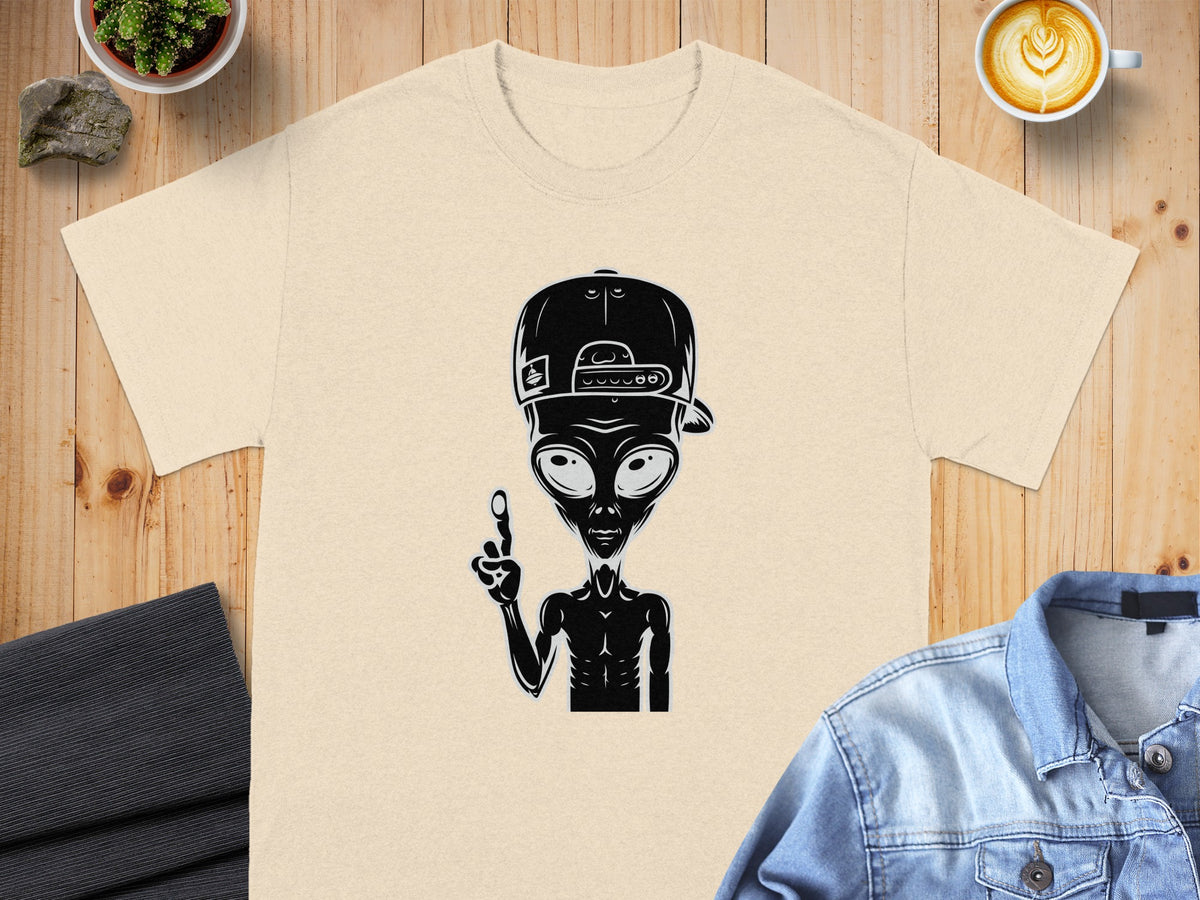 Light tan t-shirt with black alien wearing a baseball cap and pointing finger graphic.