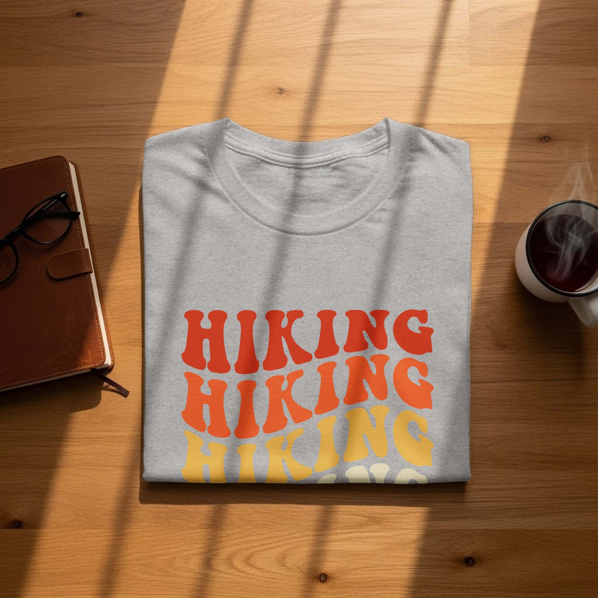 Folded grey t-shirt with orange and yellow "Hiking" text on wooden surface.