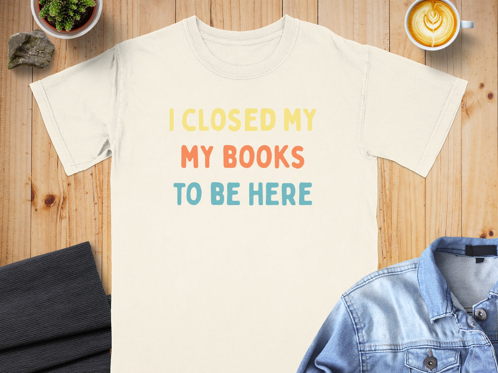 Cream t-shirt with "I CLOSED MY MY BOOKS TO BE HERE" text in yellow, coral, and blue.