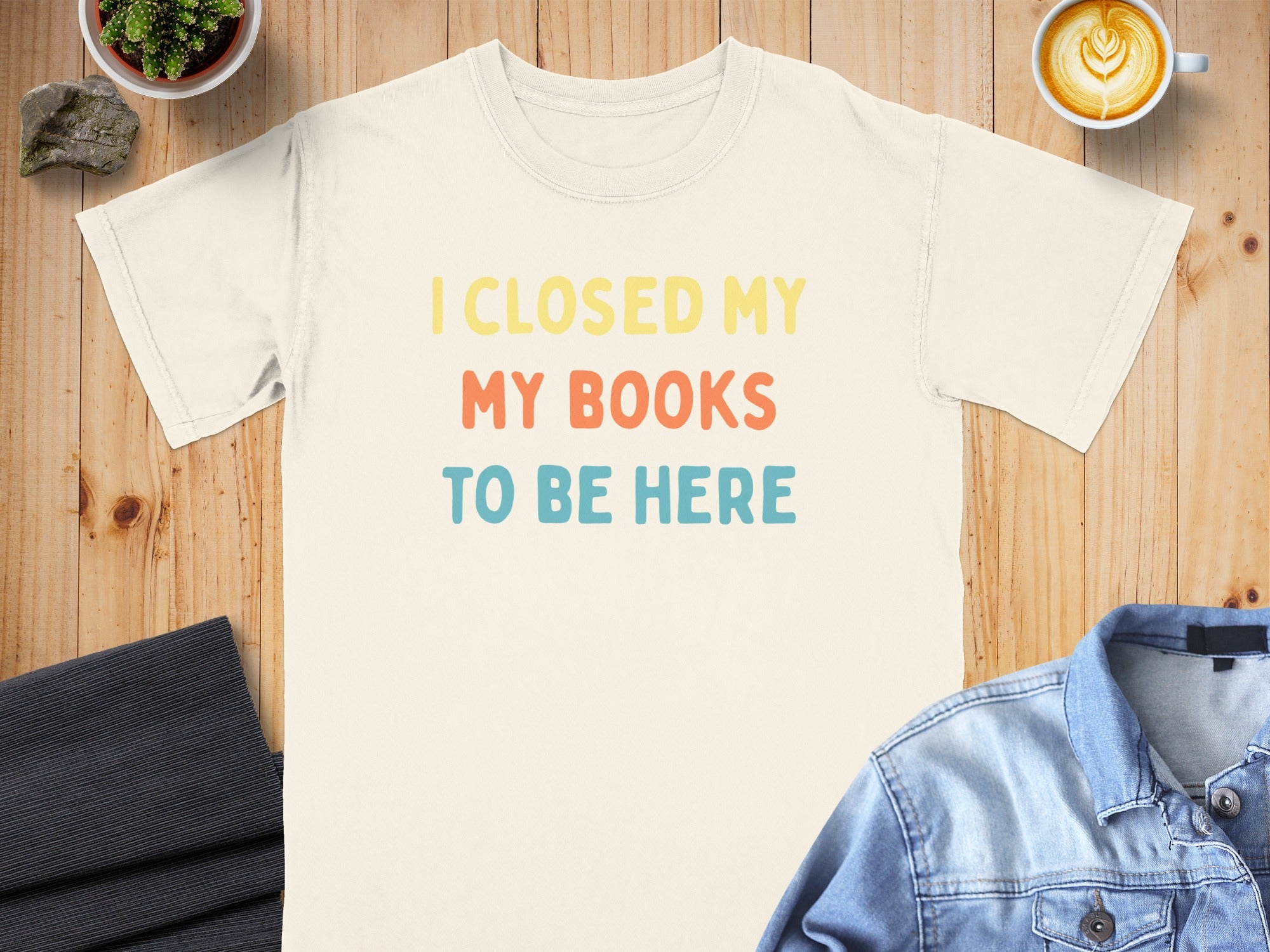 Cream t-shirt with "I CLOSED MY MY BOOKS TO BE HERE" text in yellow, coral, and blue.