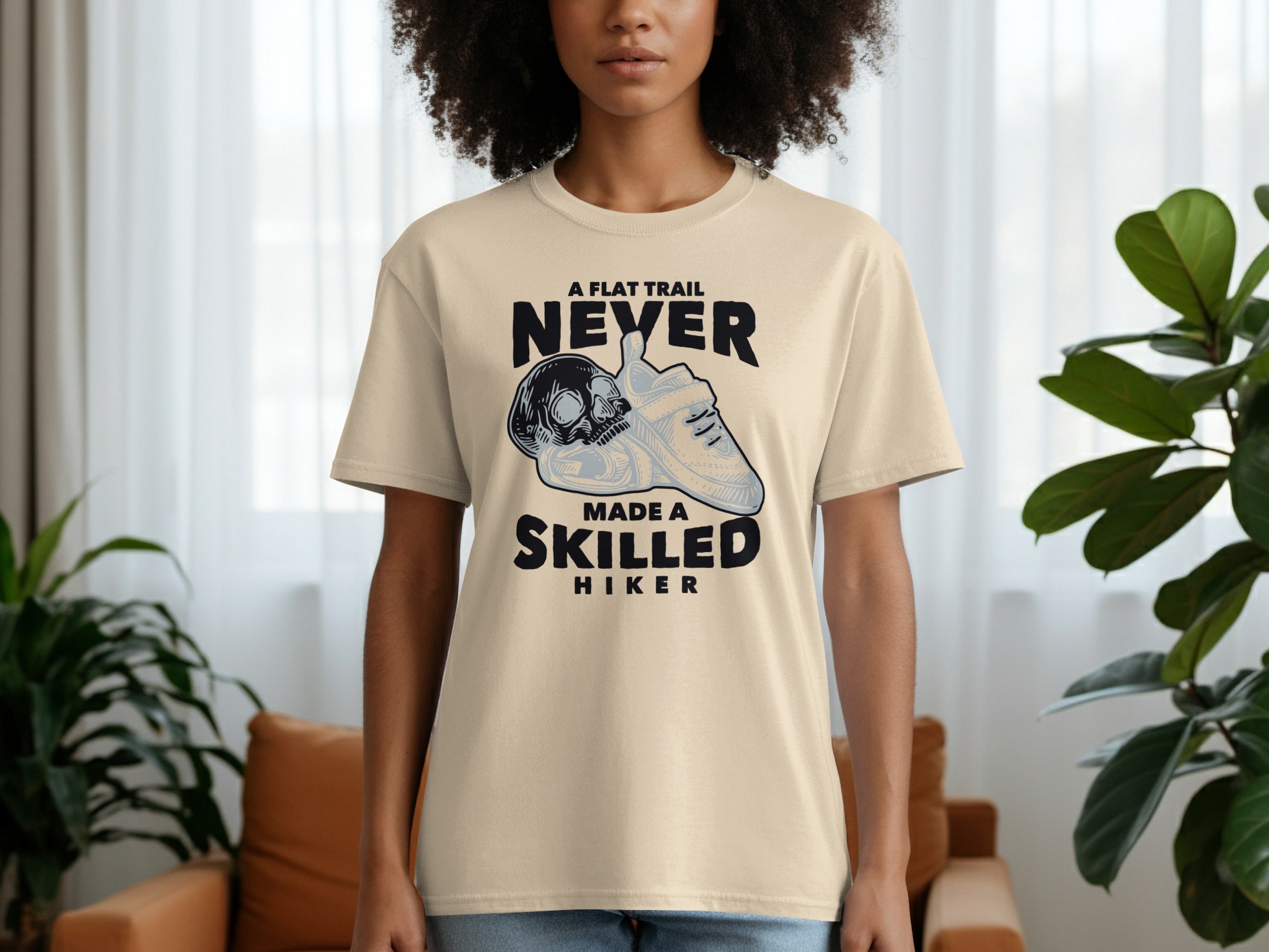 Cream t-shirt with graphic of skull and shoe, text reads "A flat trail never made a skilled hiker".