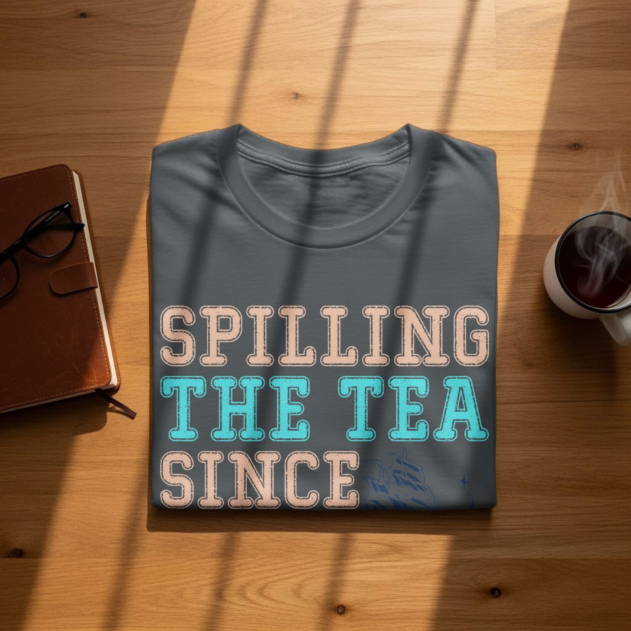 Dark grey t-shirt with "Spilling the Tea Since" in peach and teal text.