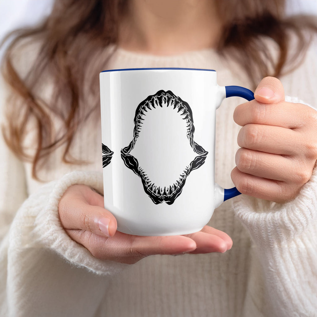 White mug with blue rim and handle featuring black shark jaw graphic.