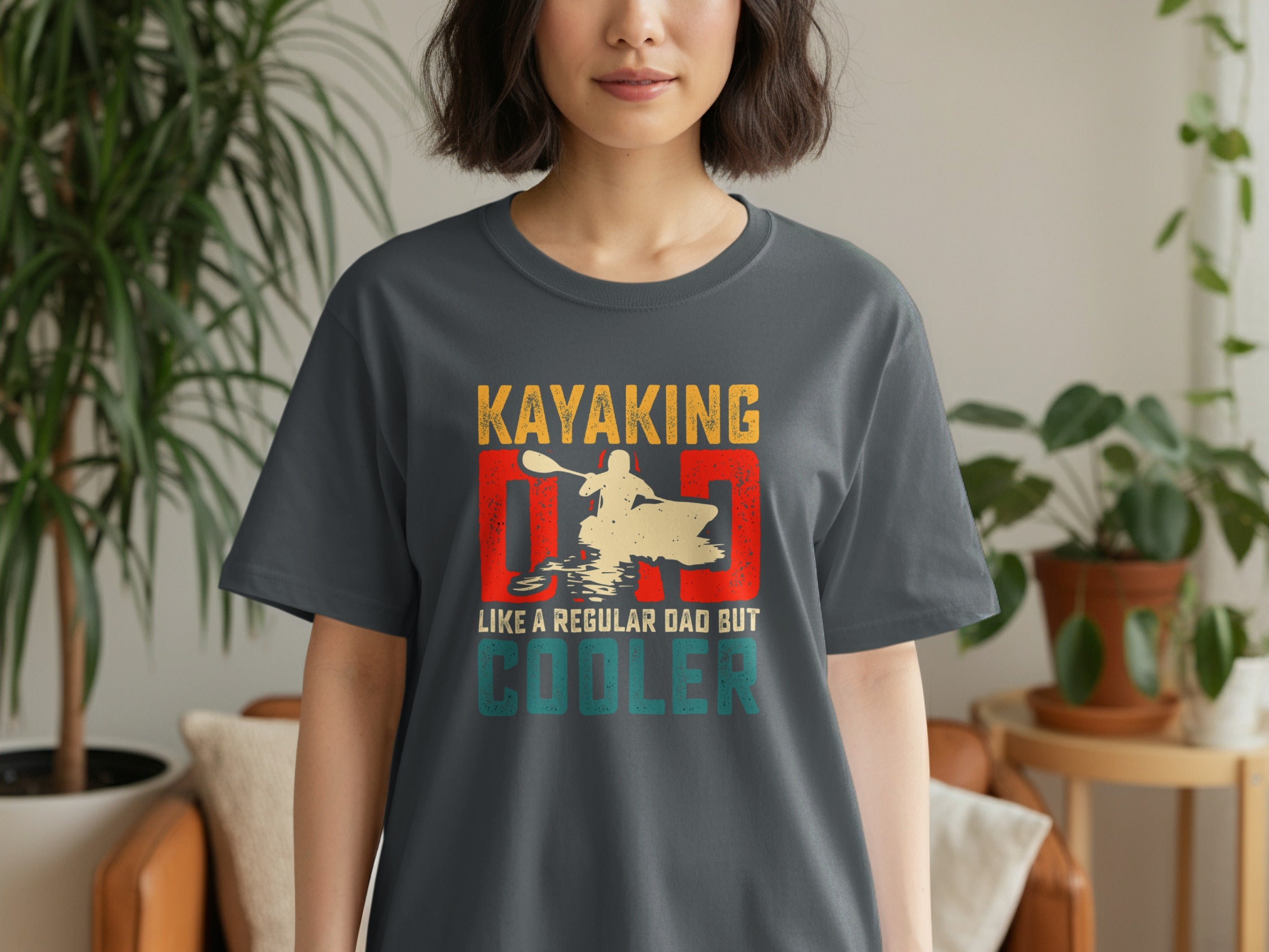 Dark grey t-shirt with text "Kayaking Like a Regular Dad But Cooler" and kayaking graphic.