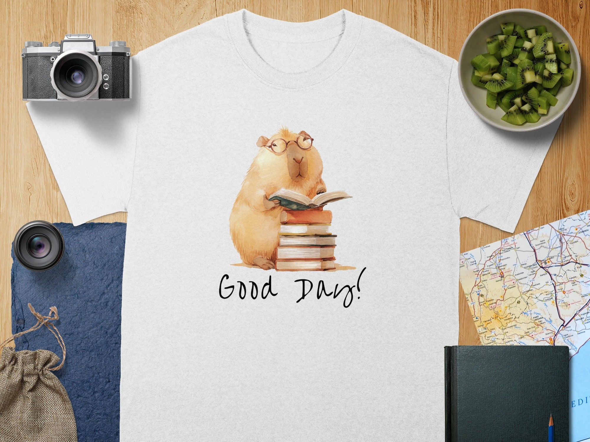 White t-shirt with watercolor capybara wearing glasses reading a book.