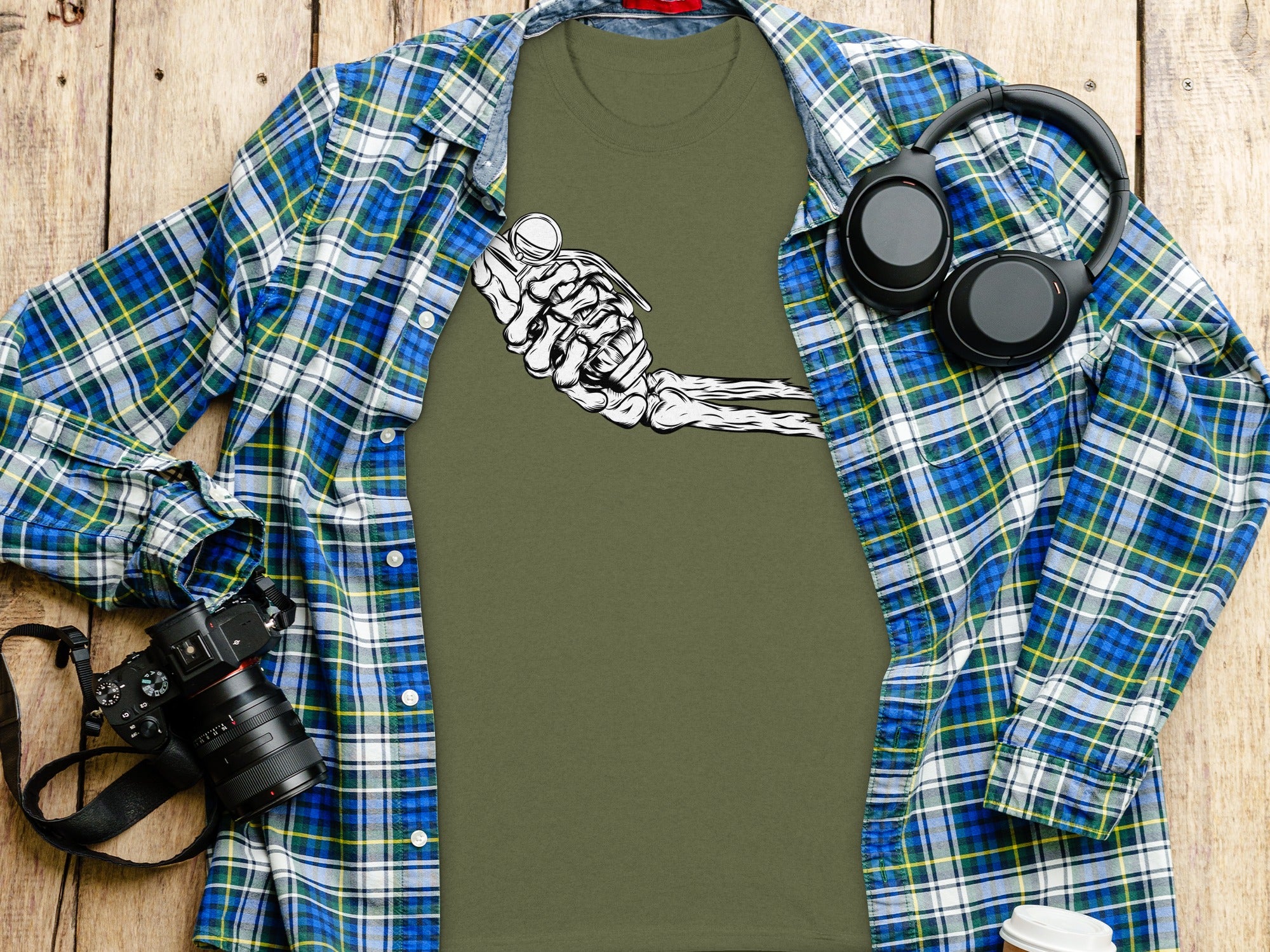 Khaki t-shirt with white skeleton hand holding grenade graphic, black headphones, and camera.