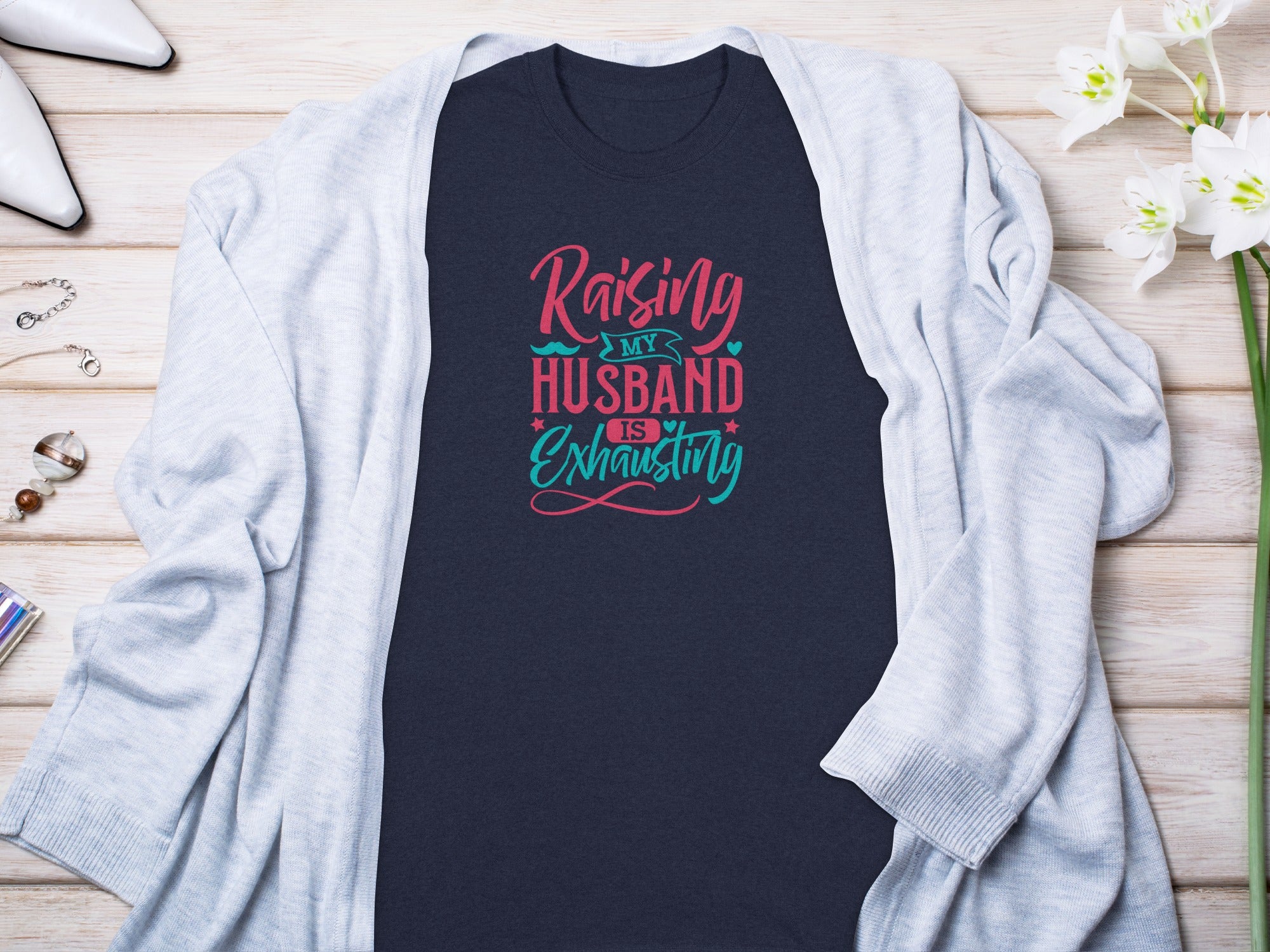Dark navy t-shirt with text "Raising my husband is exhausting" in pink and teal.